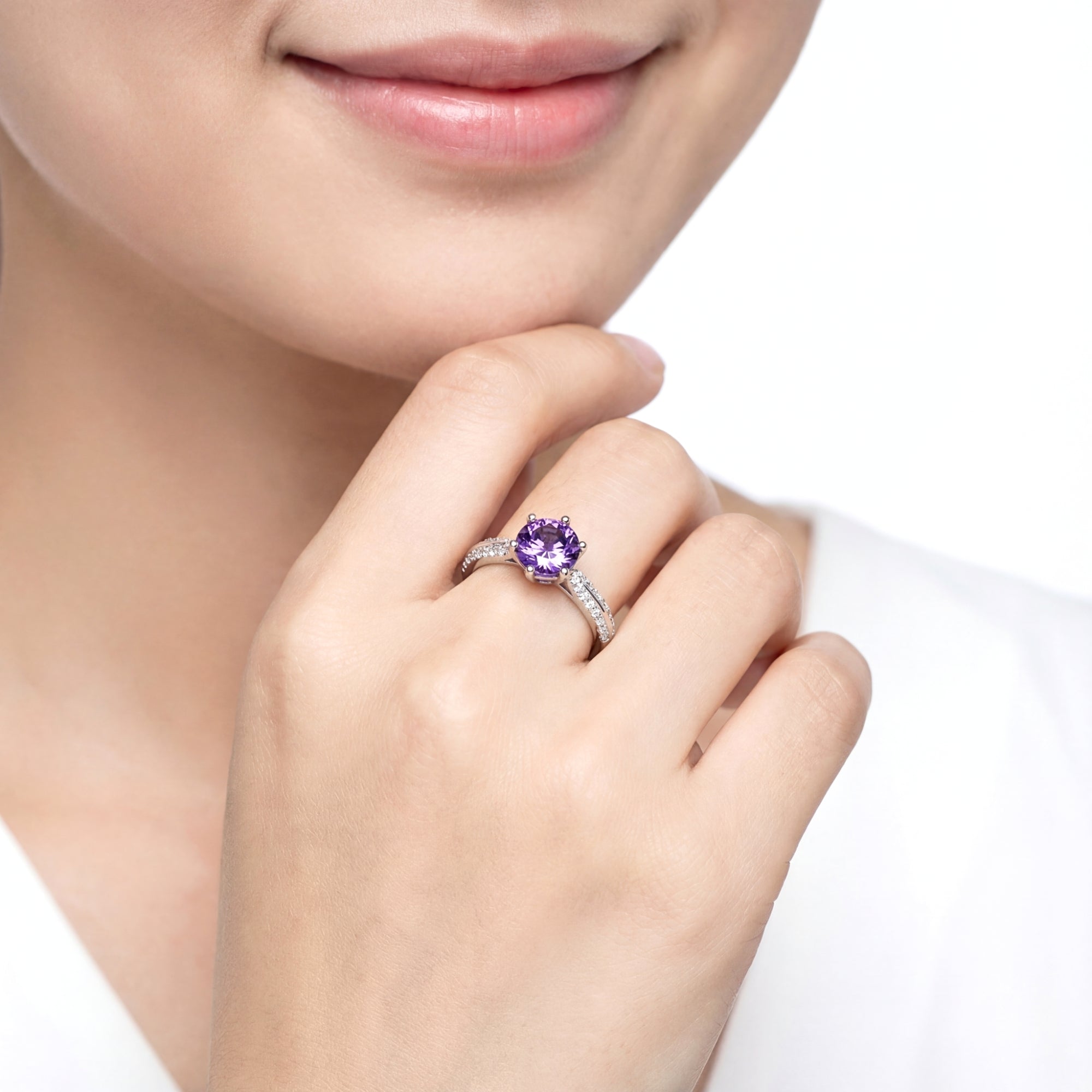 Round-cut simulated amethyst solitaire ring in sterling silver worn on a woman's hand, touching her chin.