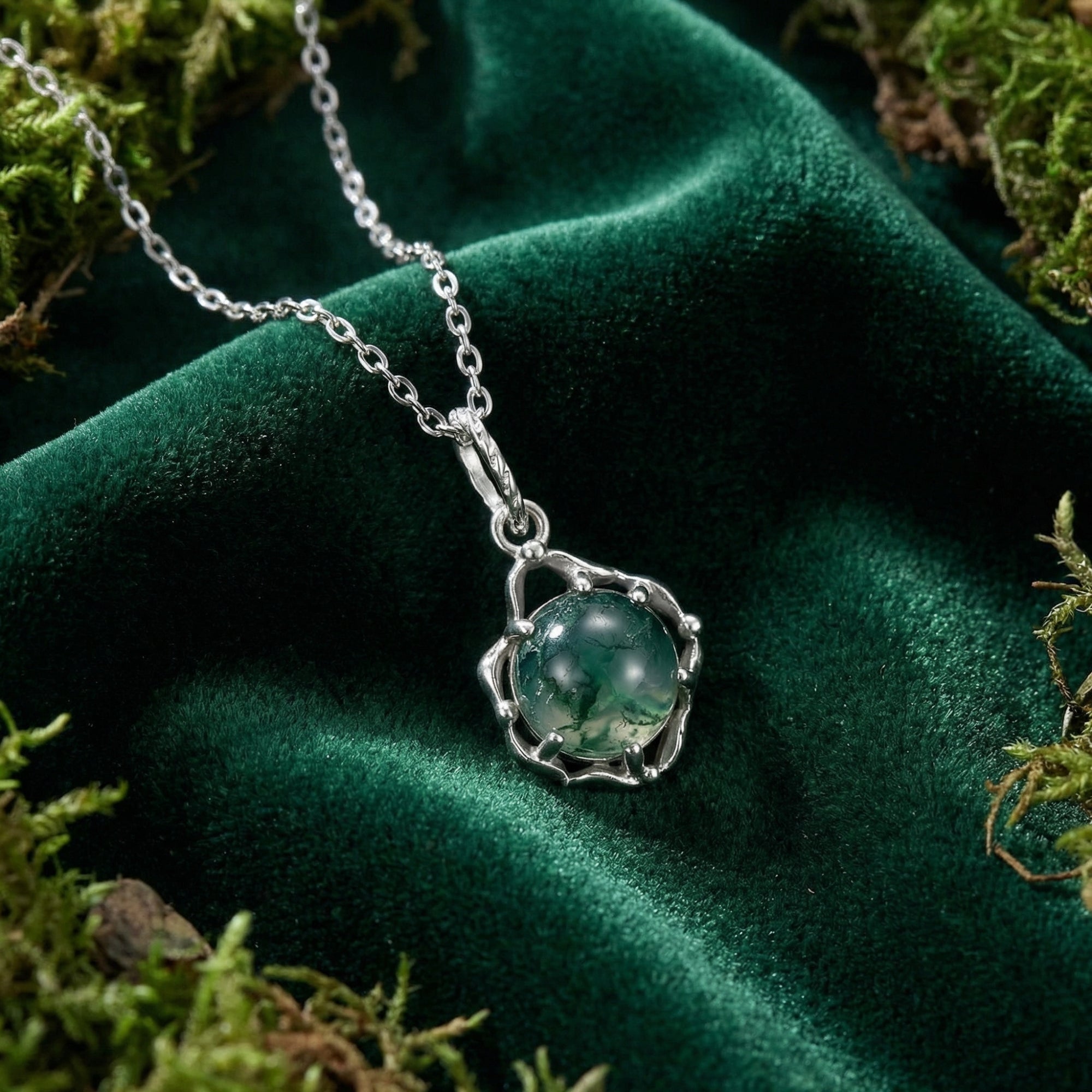 Detailed view of a round moss agate stone in a sterling silver celtic knot pendant on a dark green velvet surface.