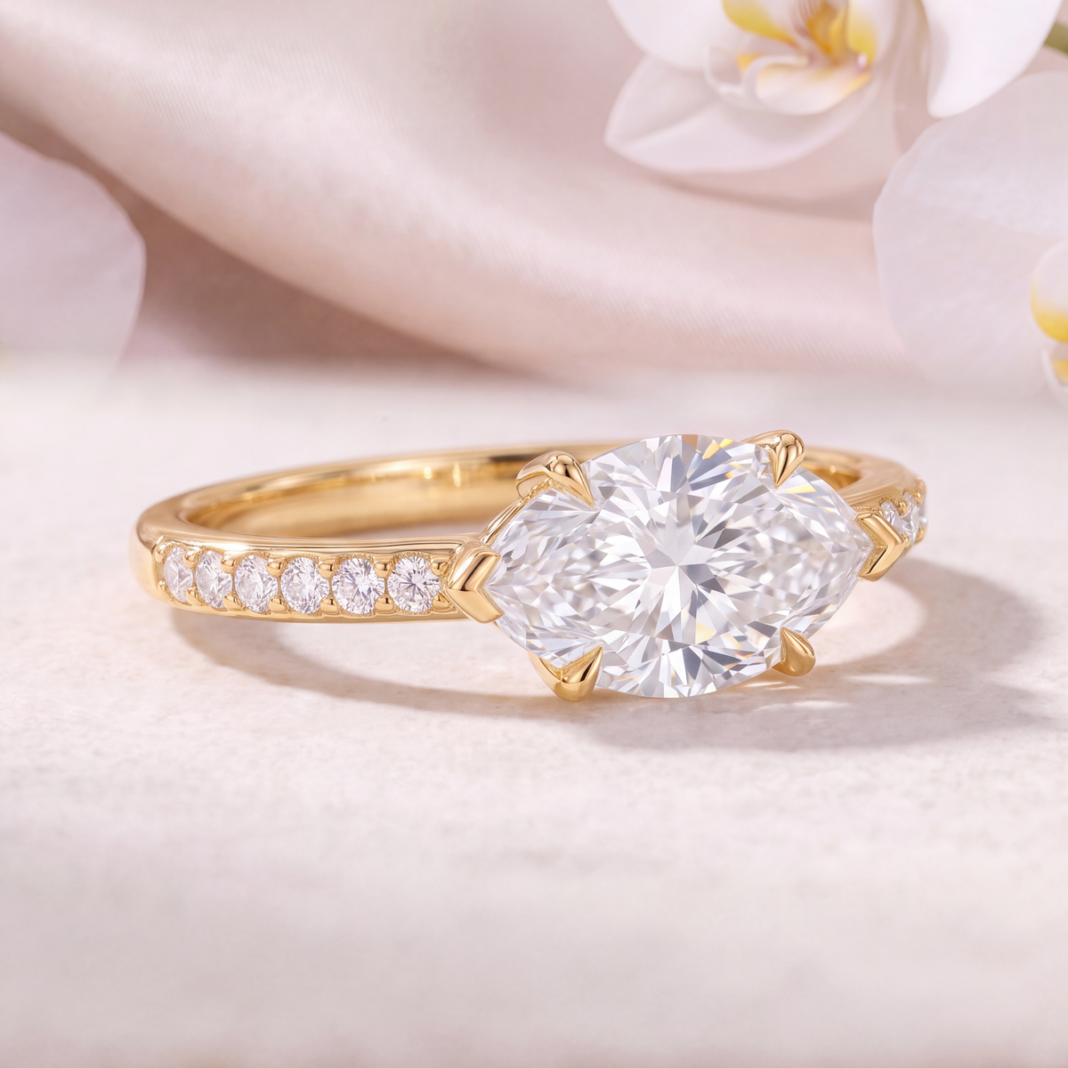Close-up angled view of a yellow gold east-west marquise moissanite ring showing the pavé band detail.