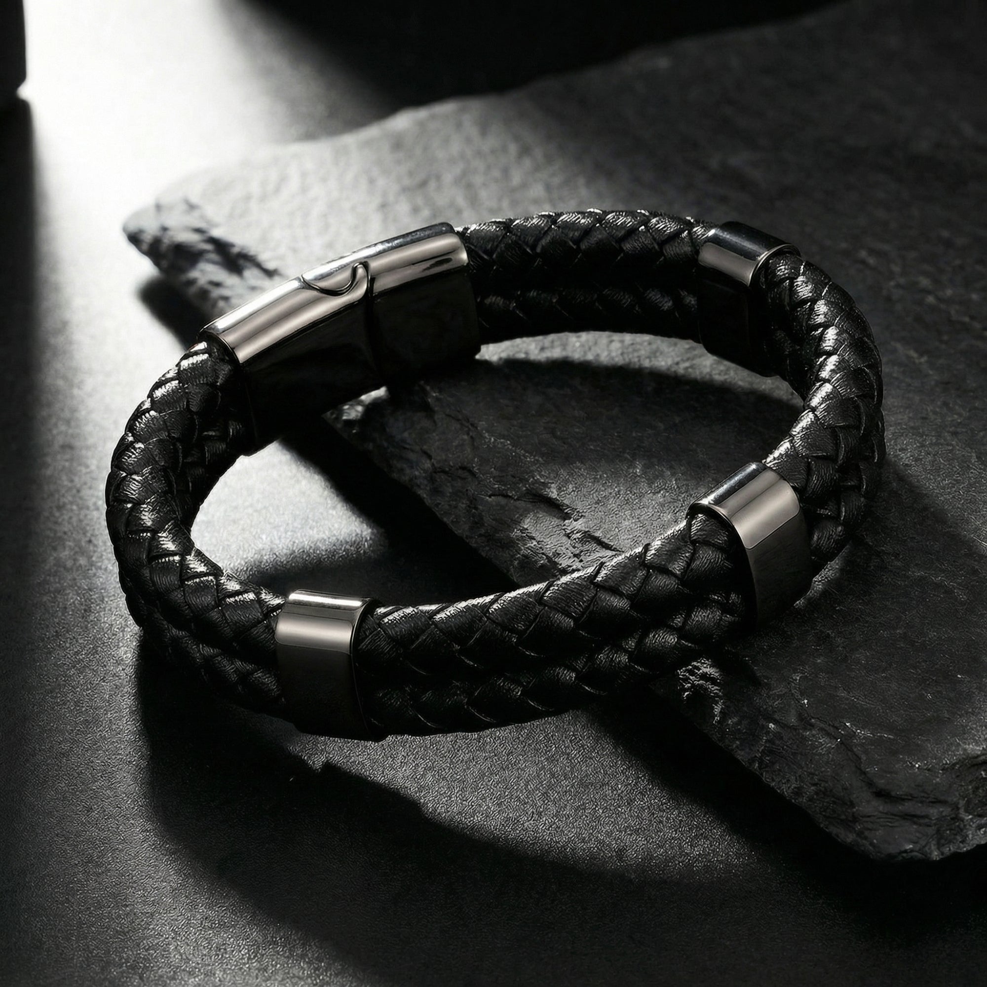 Close-up of the double-braided black leather bracelet with black stainless steel accents on a dark stone background.