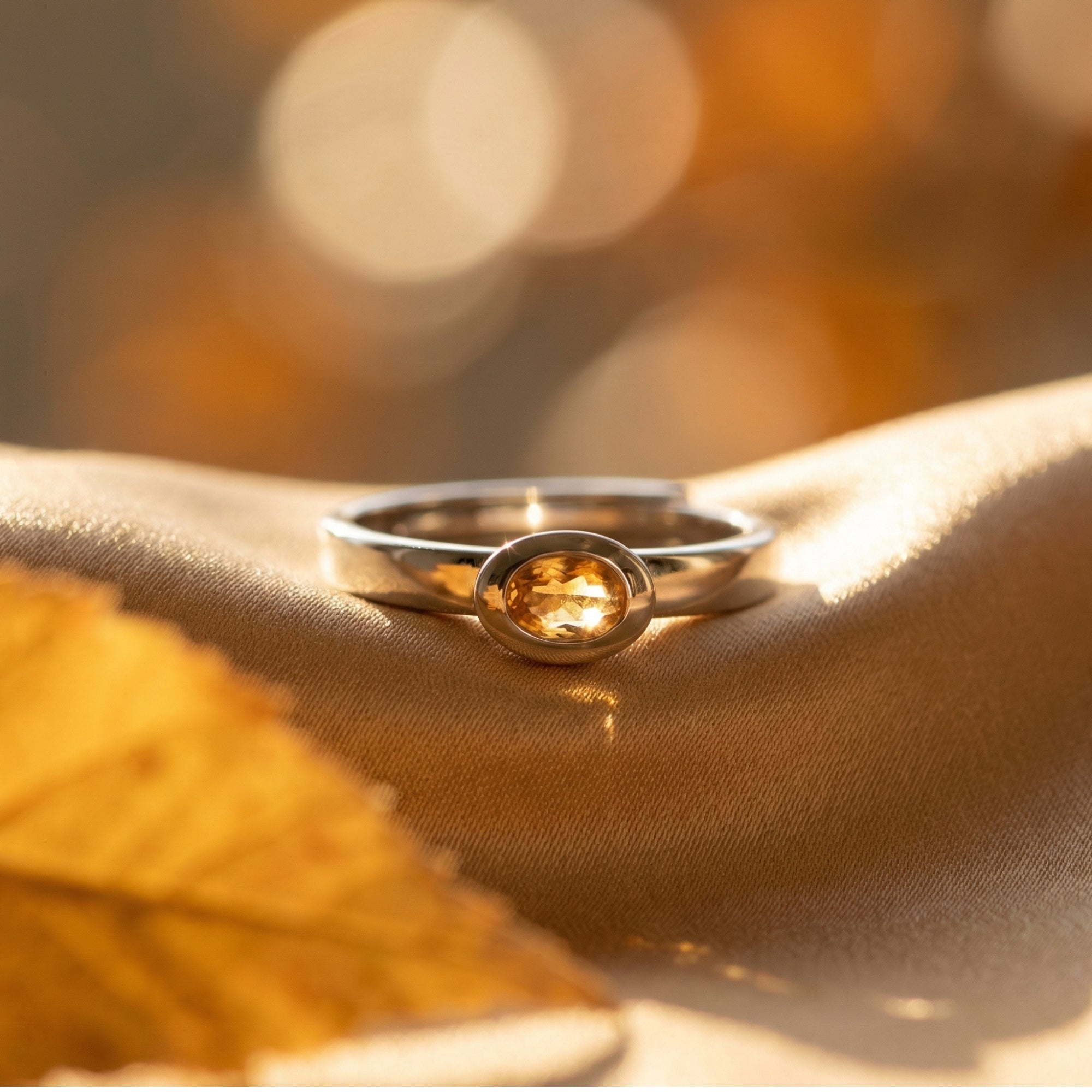 Macro view of the oval cut natural citrine gemstone and silver bezel setting on golden fabric.