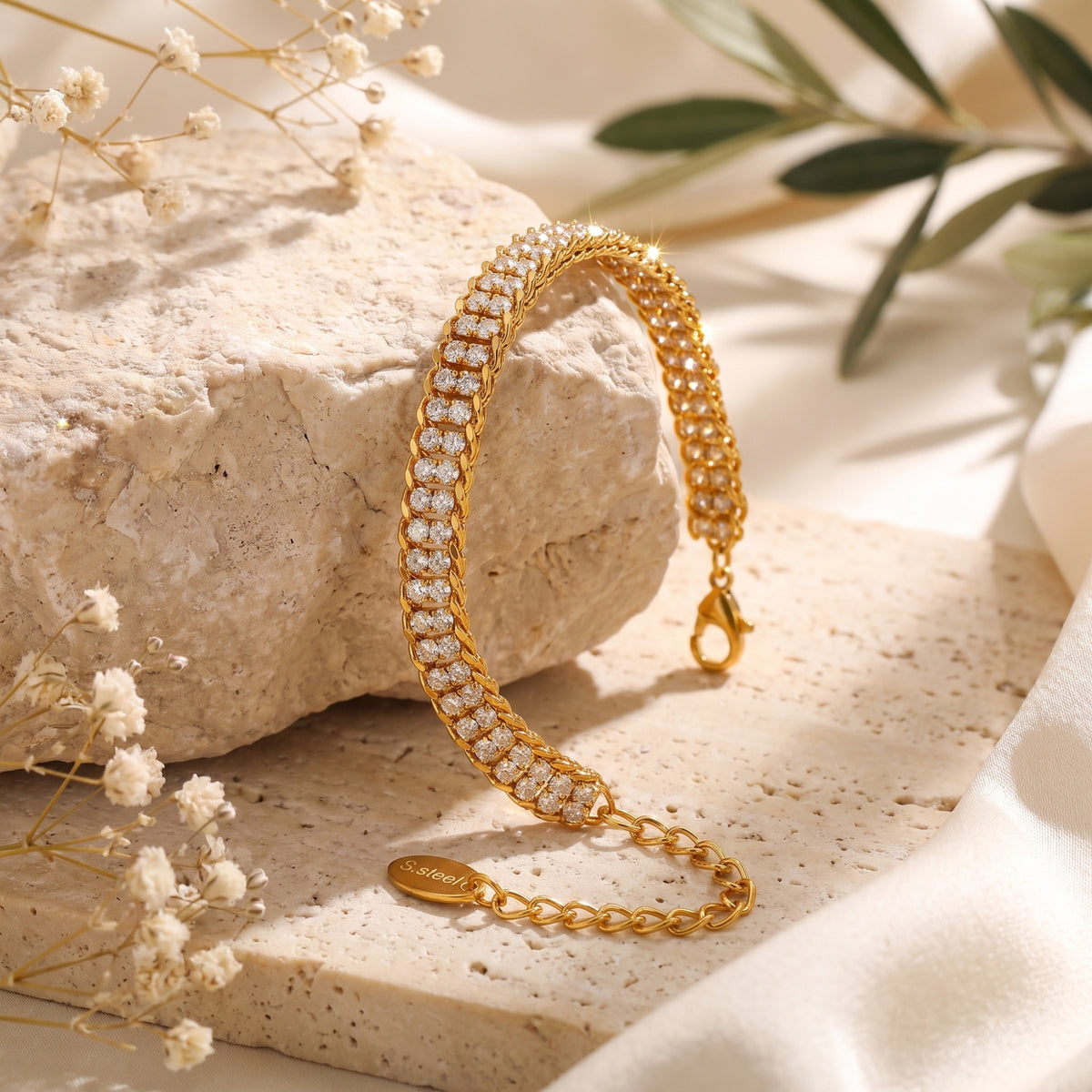 Gold-tone double-row pavé link bracelet draped over a rough stone, with clasp, extension chain, and tag visible.
