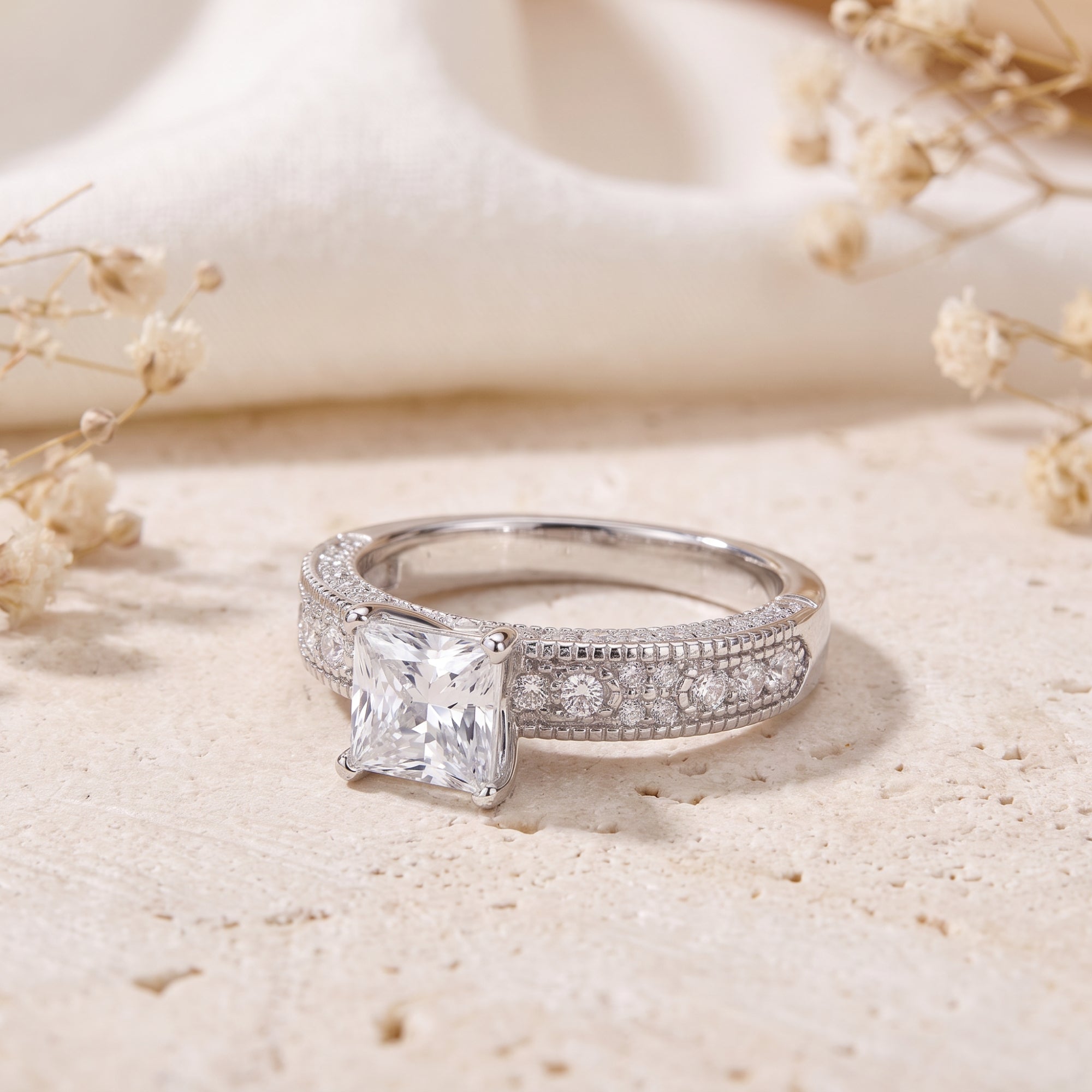 Front view of princess cut CZ silver ring on stone background.
