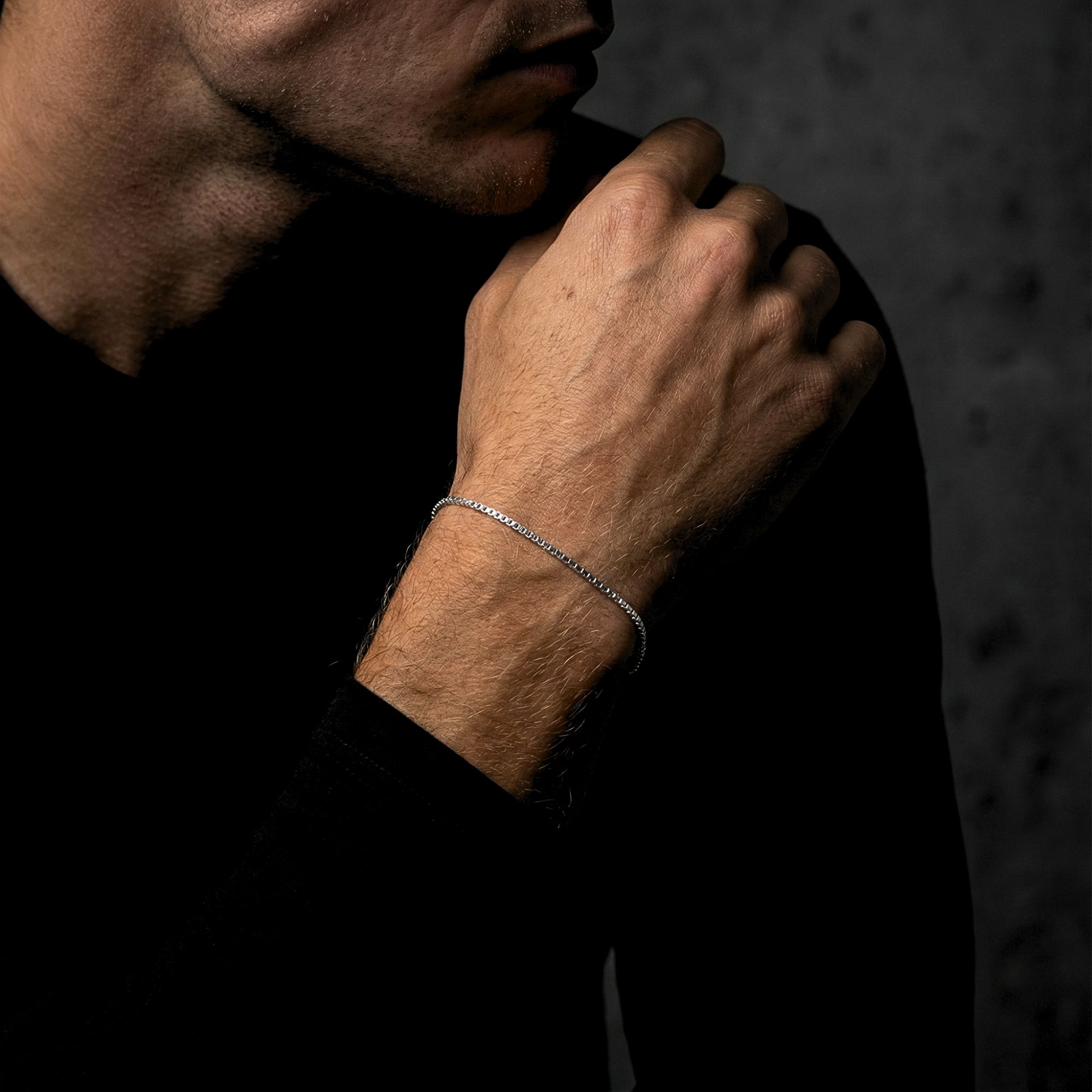 Men's silver stainless steel box chain bracelet worn on a wrist with a black long-sleeve shirt.