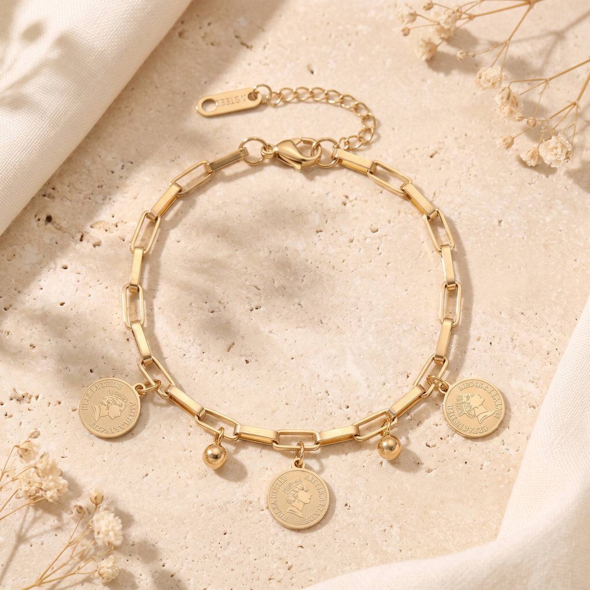 Overhead flat lay of the gold-tone paperclip chain bracelet with coin pendants and round bead charms.