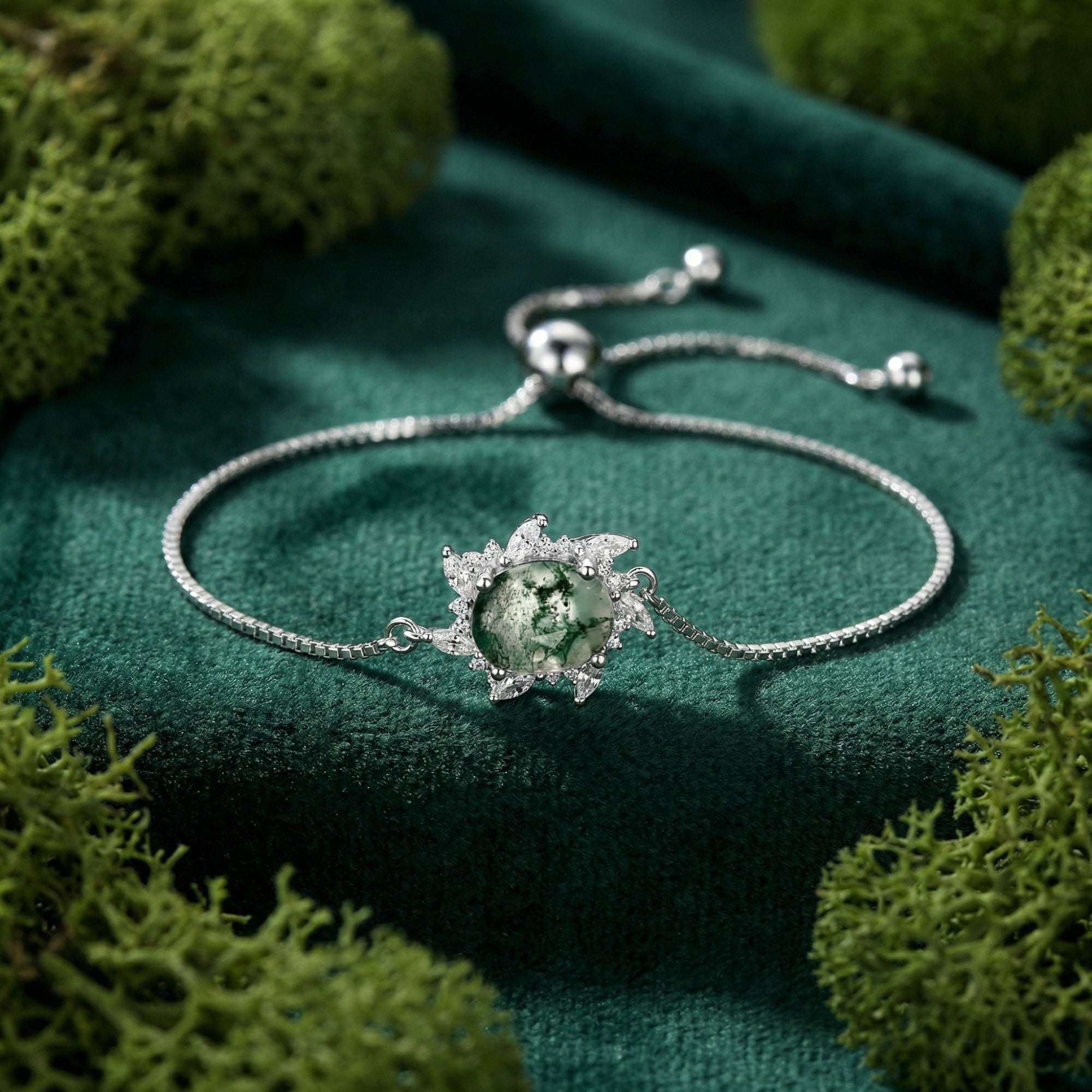 Close-up of a round natural moss agate stone in a sunburst sterling silver setting on green velvet.