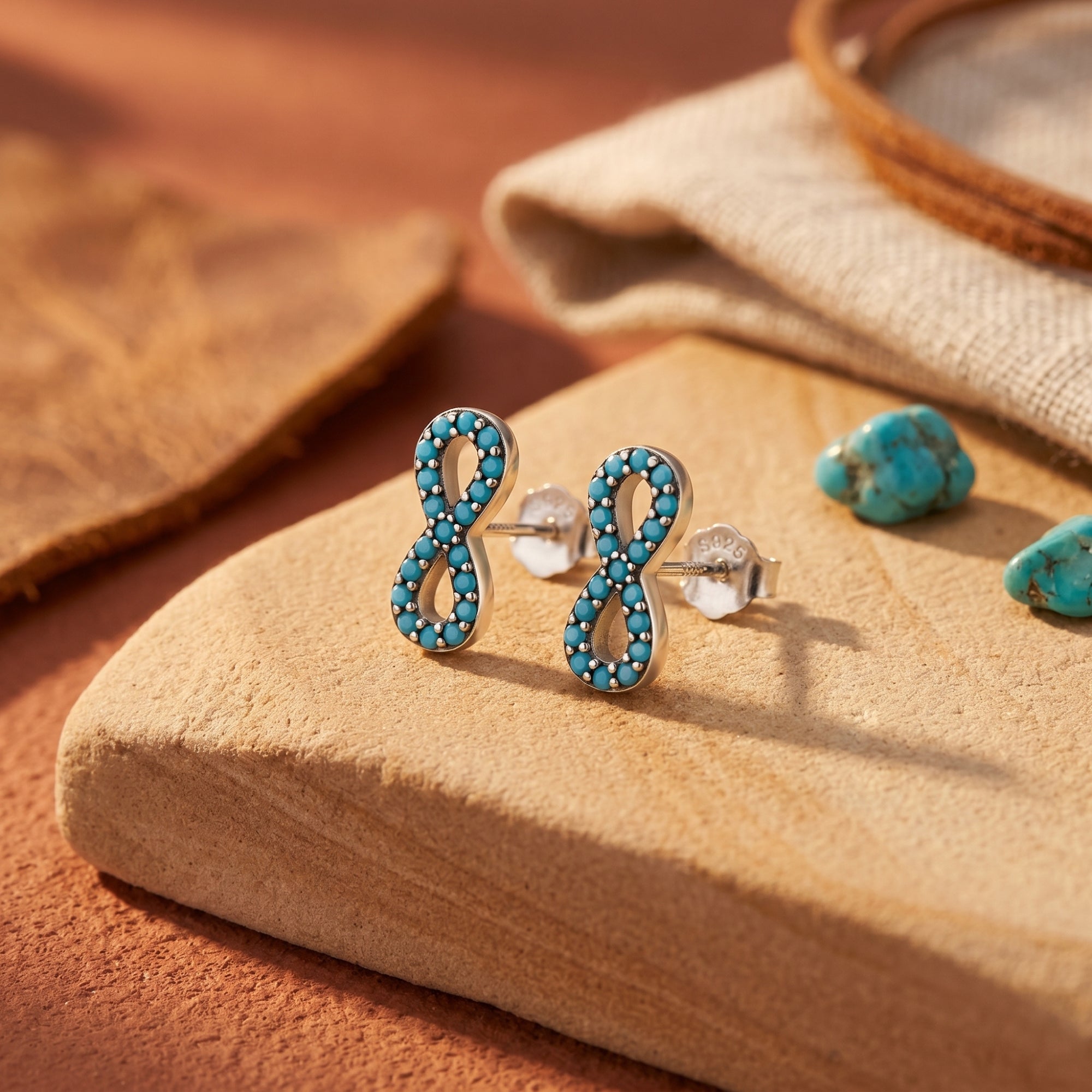 Close-up of silver infinity earrings with hand-set turquoise stones on a textured stone background.