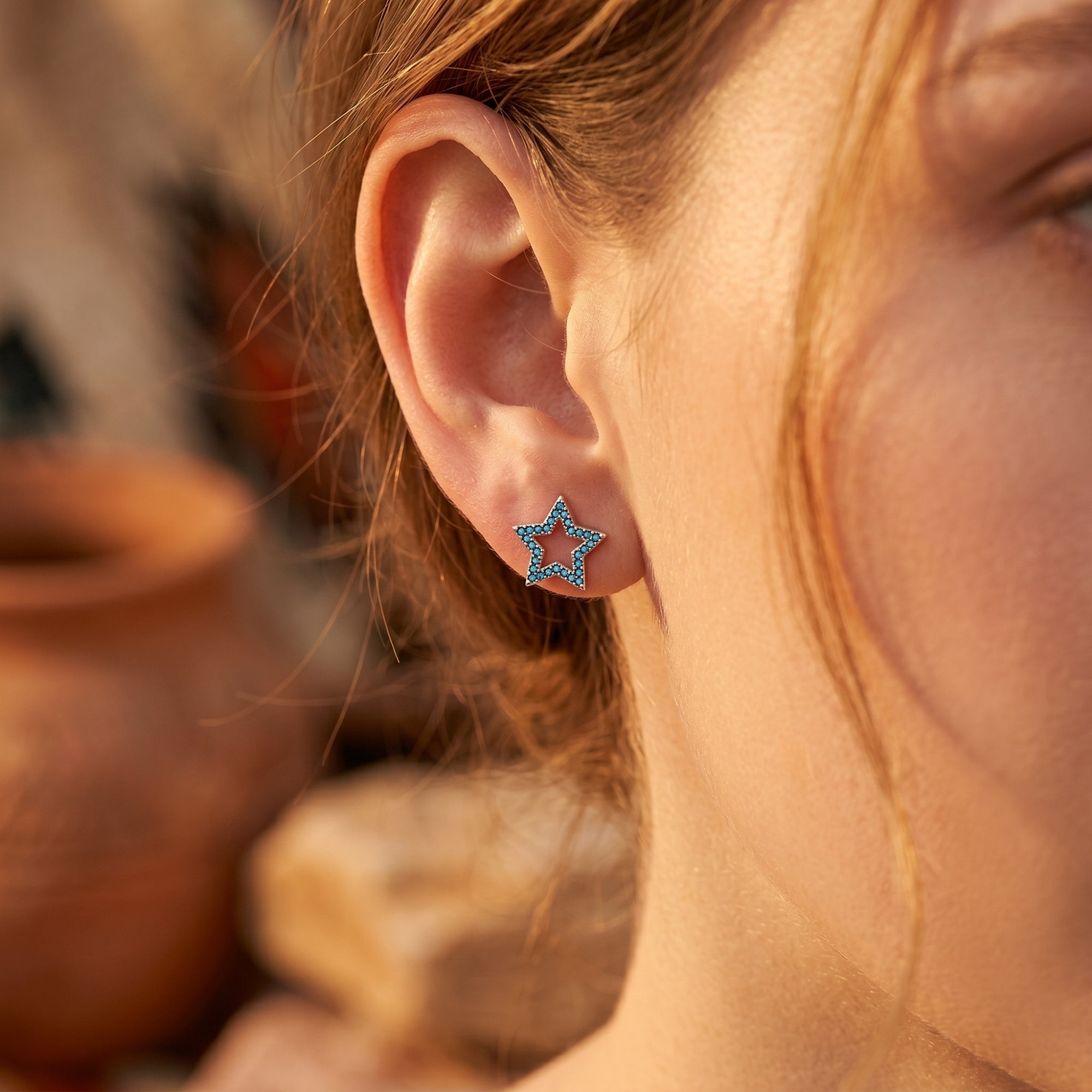 Model wearing a sterling silver star earring with turquoise pave stones, showcasing the December birthstone.