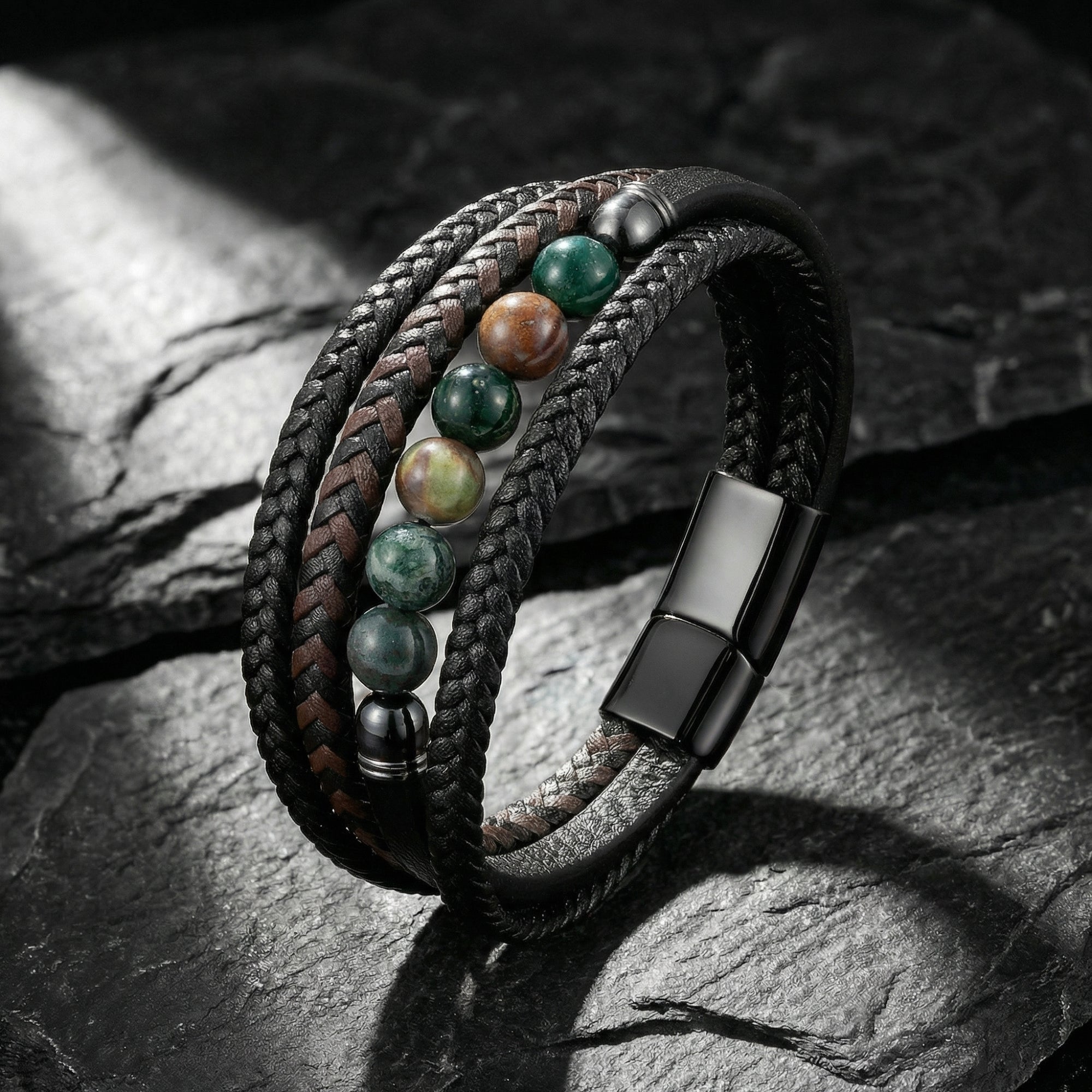 Shadow Weave leather bracelet with round green and brown stone beads and black stainless steel clasp on a stone surface.