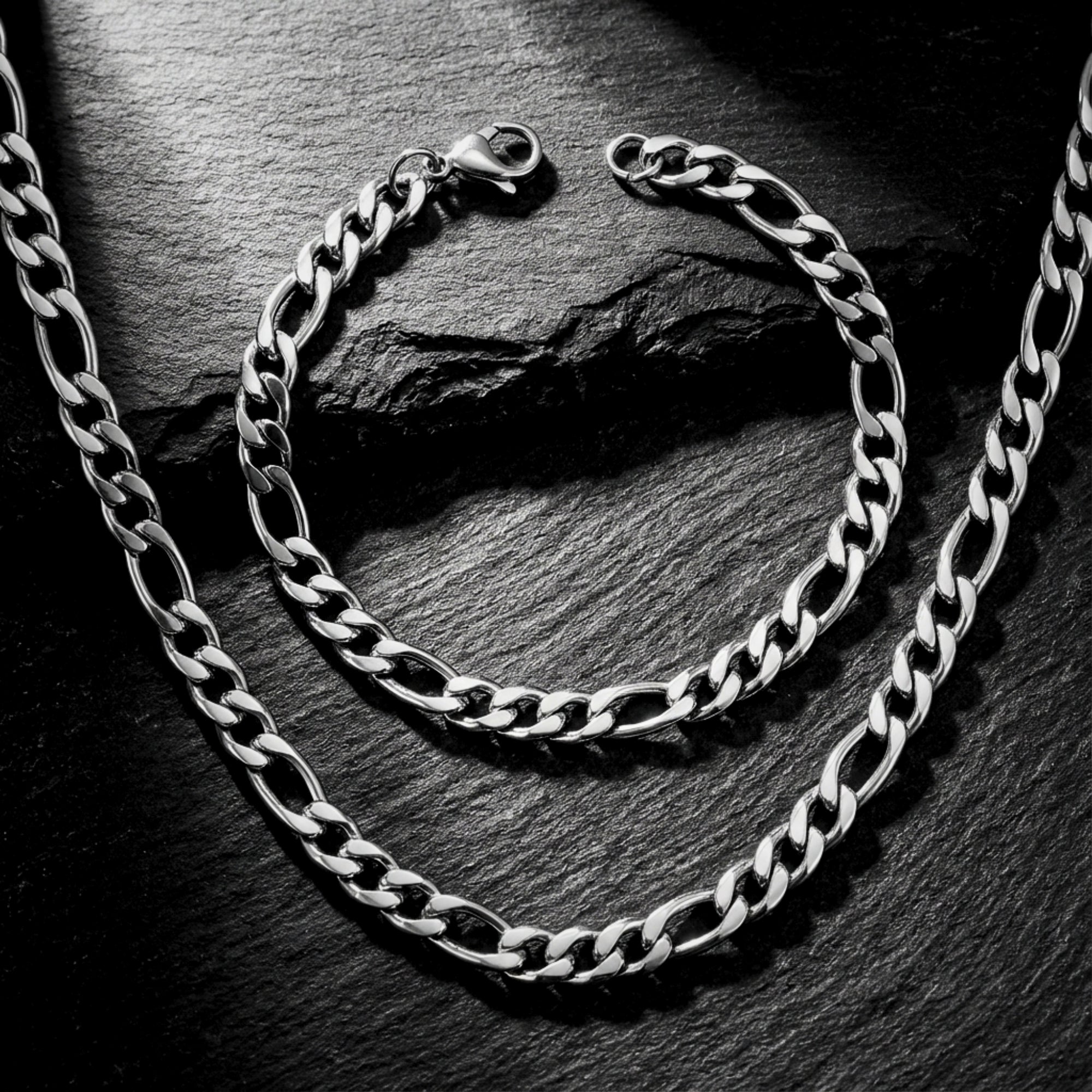 Close-up of polished silver 8mm Figaro links and lobster clasp on a stainless steel chain and bracelet set.