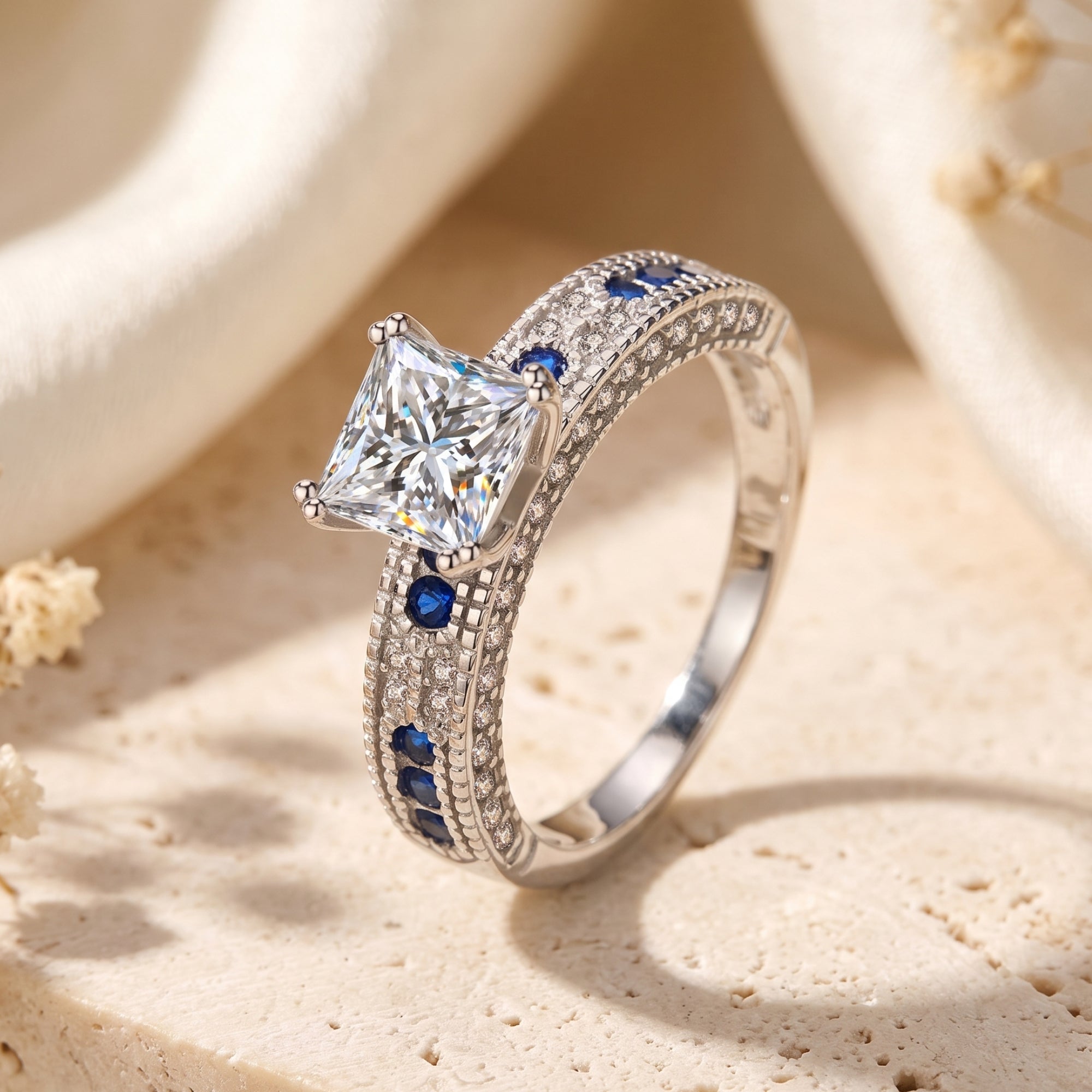 Angled view of a silver princess-cut CZ ring with blue sapphire side stones.