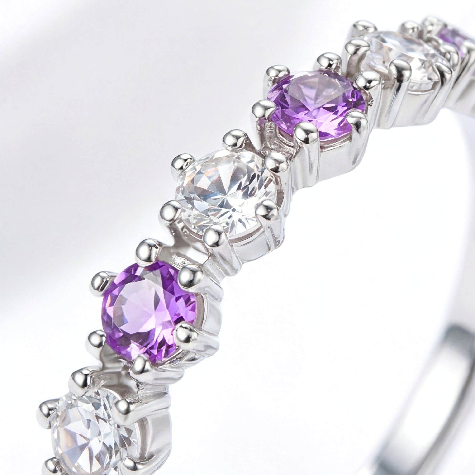 Macro view of round-cut simulated amethysts and clear stones in a sterling silver prong setting.