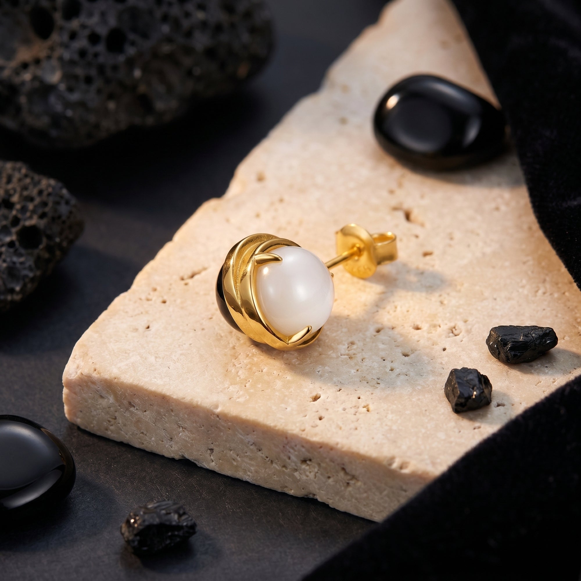 Close-up of an 18K gold plated Ravenna earring with a round white chalcedony stone on a natural stone surface.