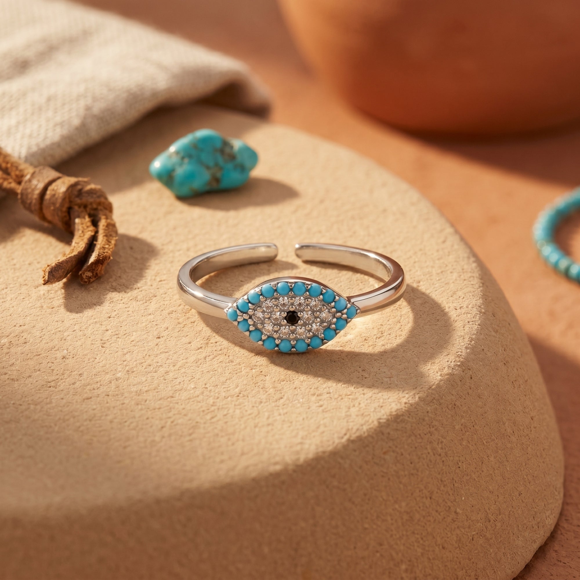 Close-up of the Samira ring's turquoise evil eye motif and silver adjustable band on a textured surface.