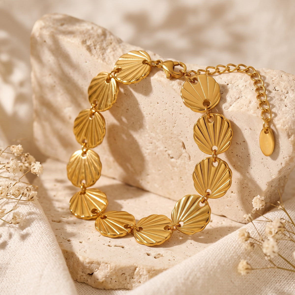 Gold-tone seashell link bracelet arranged over a raised textured stone block with dried flowers