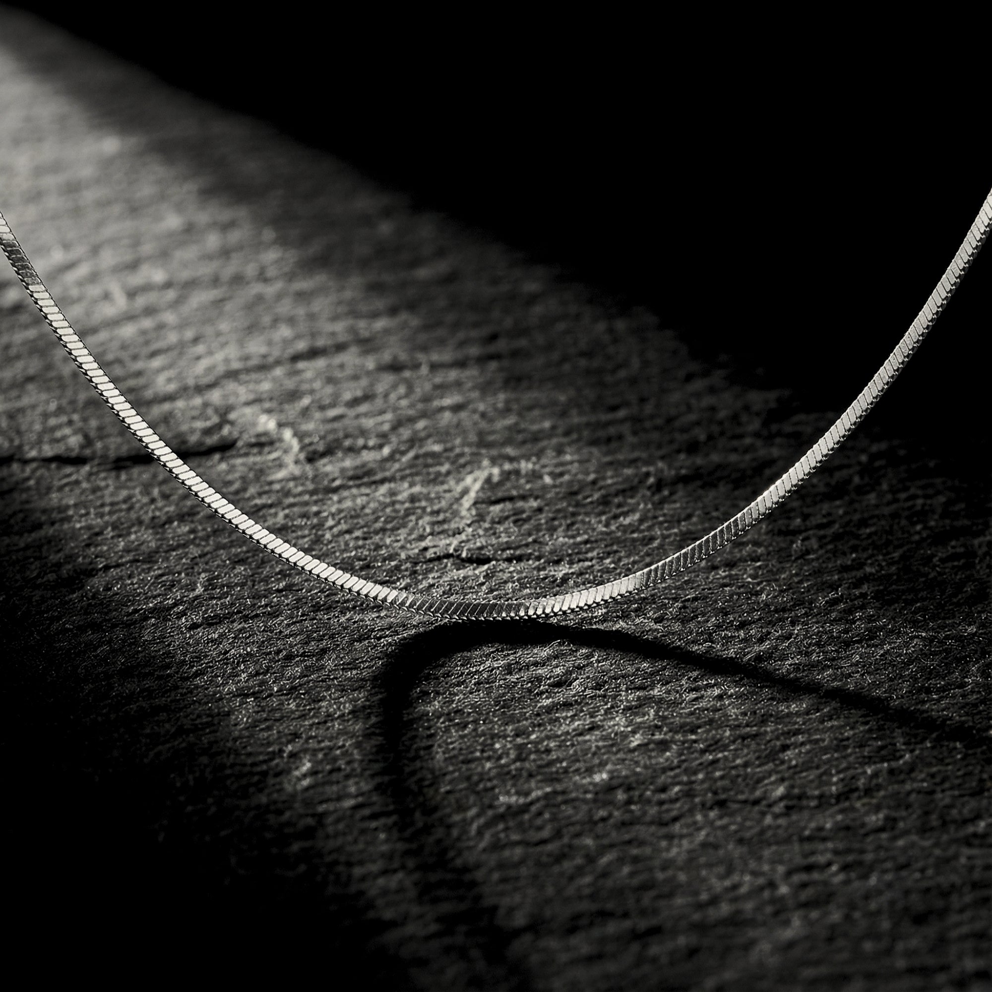 Macro view of a silver stainless steel square link chain highlighting the modern, minimalist link texture.