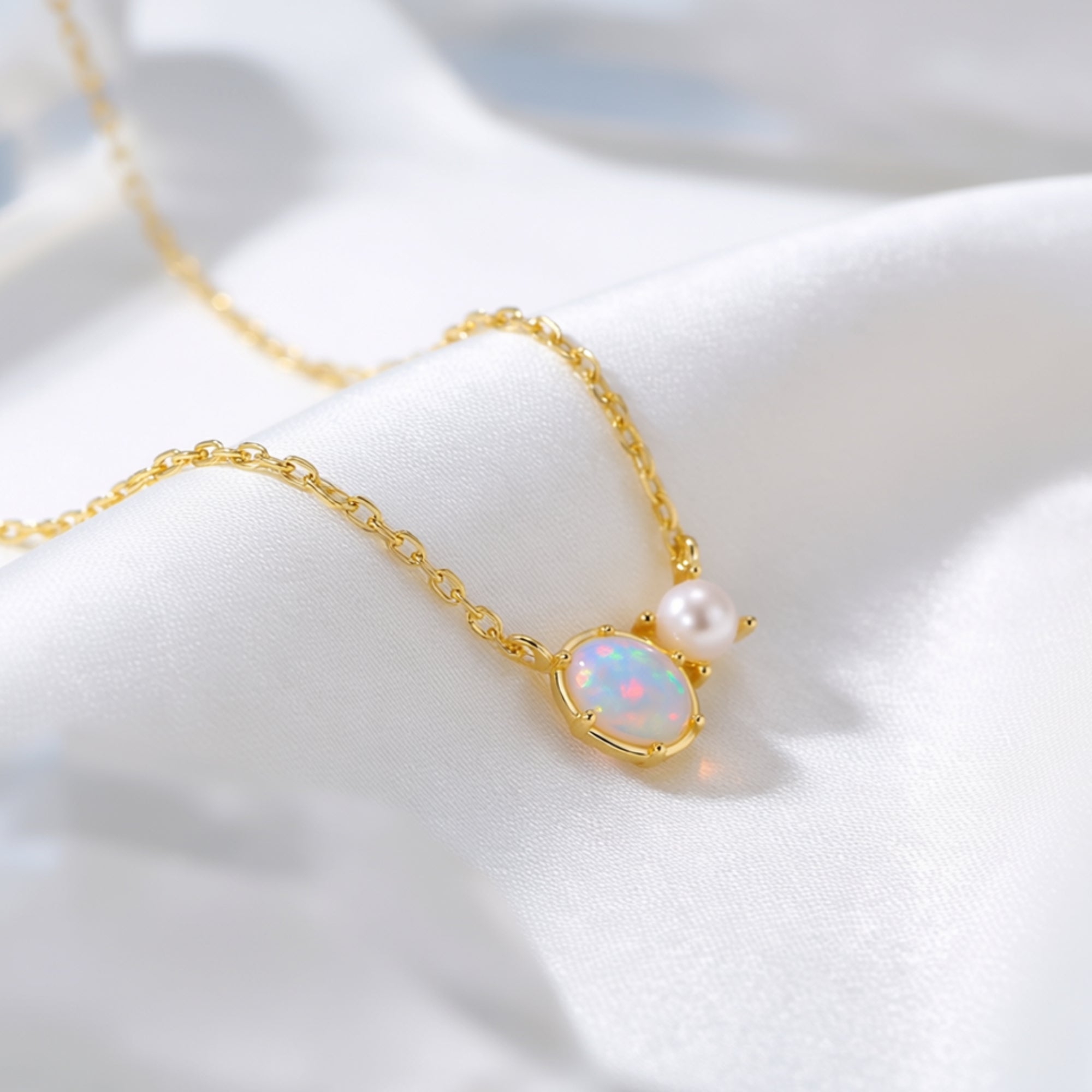 Macro view of a gold oval white opal and round pearl pendant on a dainty chain.