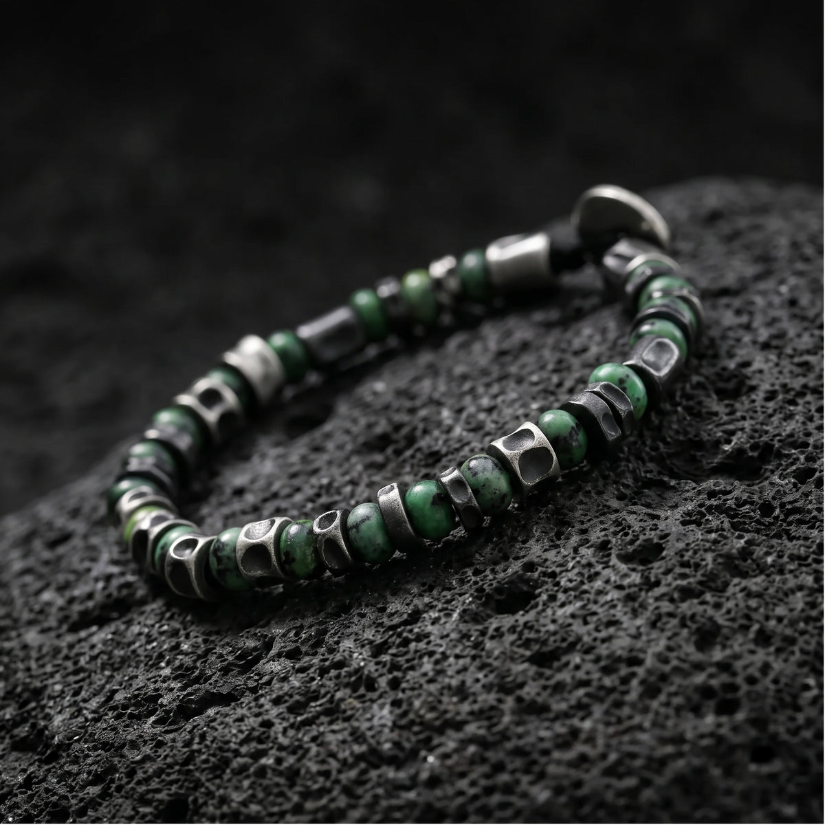 Angled close-up of the green stone and silver barrel spacer bracelet resting on porous lava rock.