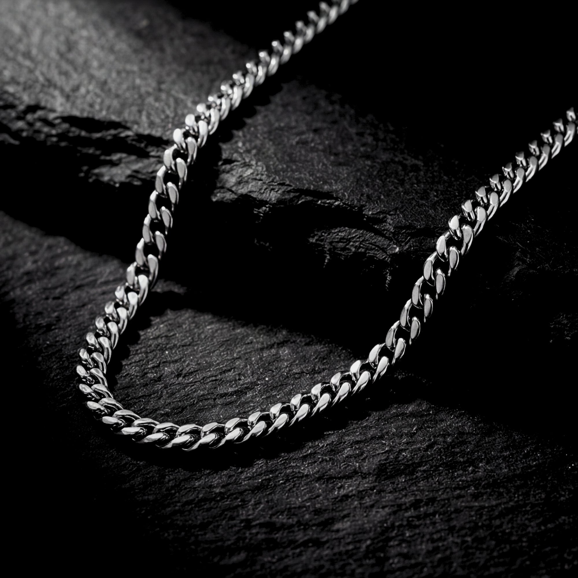 Macro detail of the links on a 4mm silver Miami Cuban stainless steel chain against a dark stone background.