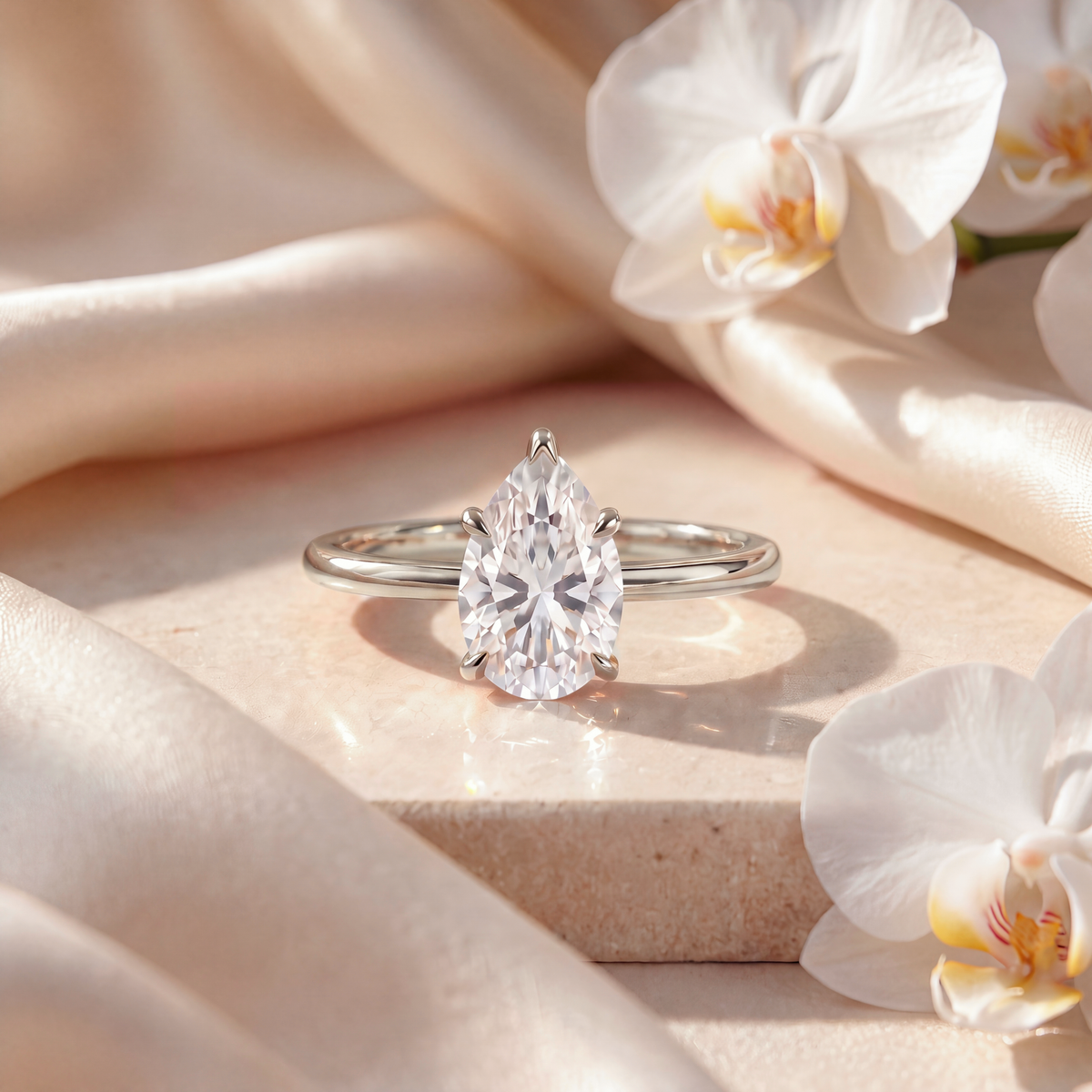 A pear-cut moissanite solitaire ring in white gold displayed on a marble surface.