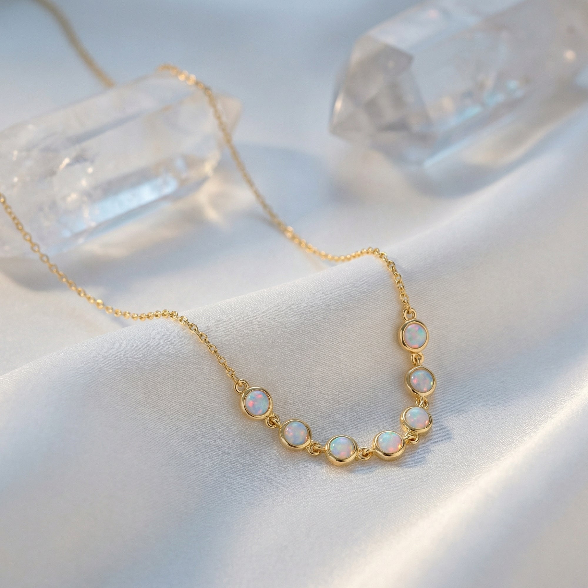 Seven round-cut white opals in gold-tone bezel settings on the Lumina necklace, displayed on white satin.