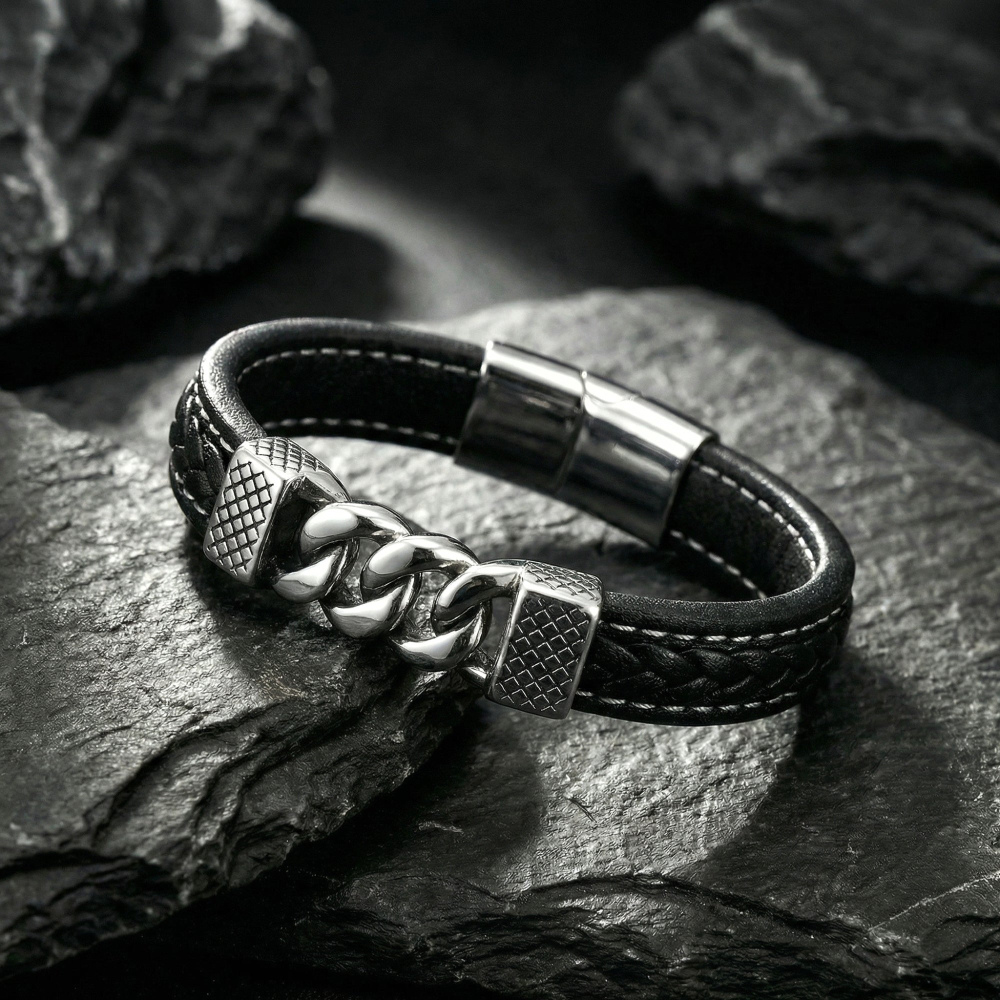 Macro view of the silver stainless steel interlocking links on a braided black leather bracelet over dark rocks.