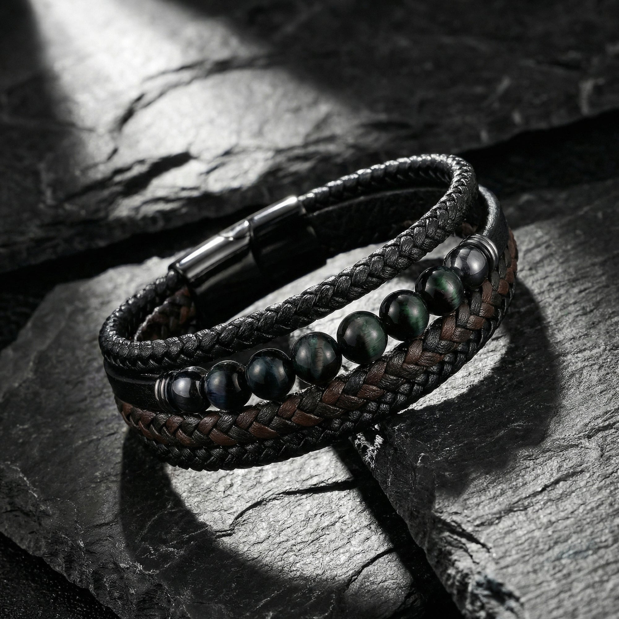 Close-up of a multi-layered braided leather bracelet with black stainless steel clasp and round green beads on stone.
