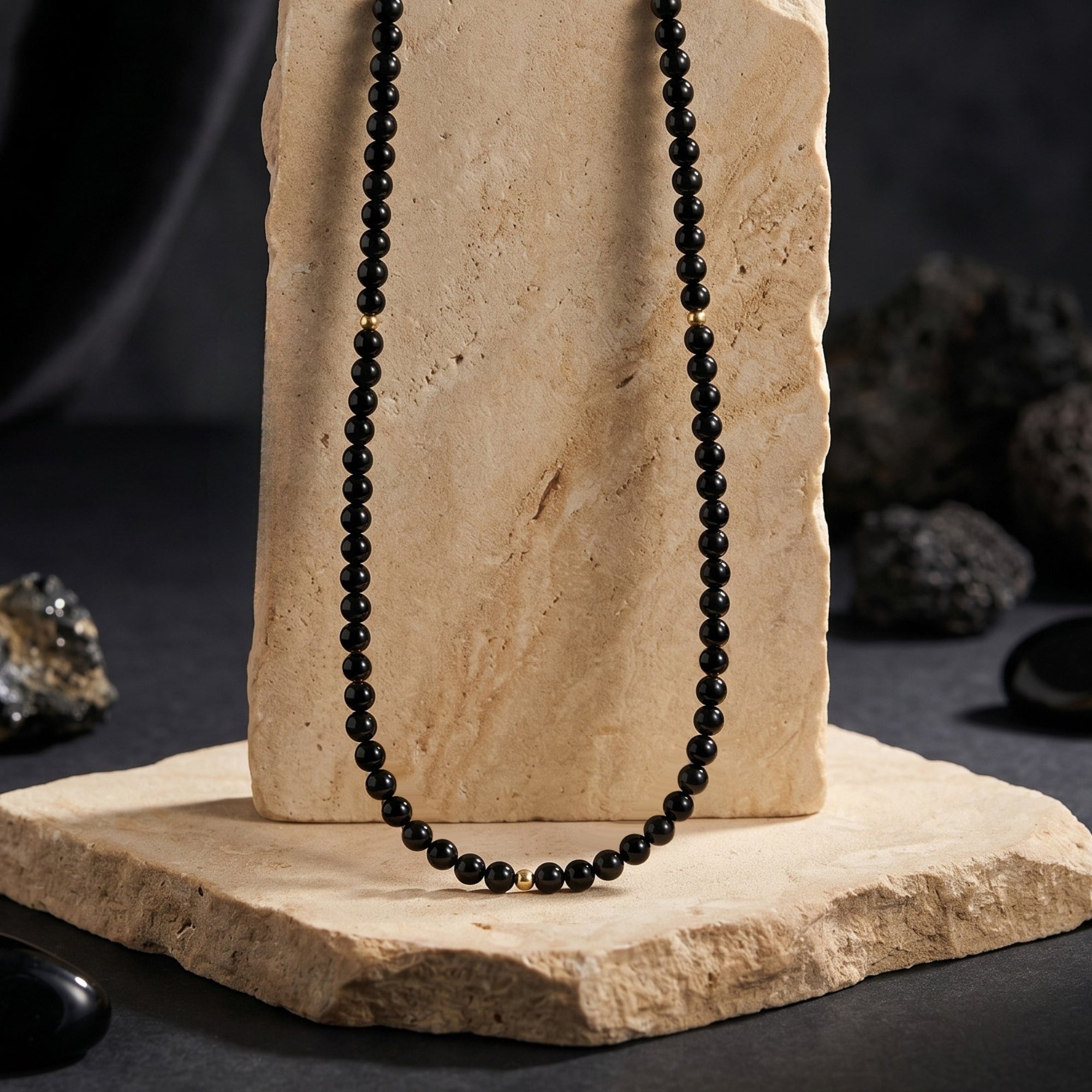 Vertical view of the 3mm polished black onyx bead necklace with 18K gold accents displayed on a textured stone block.