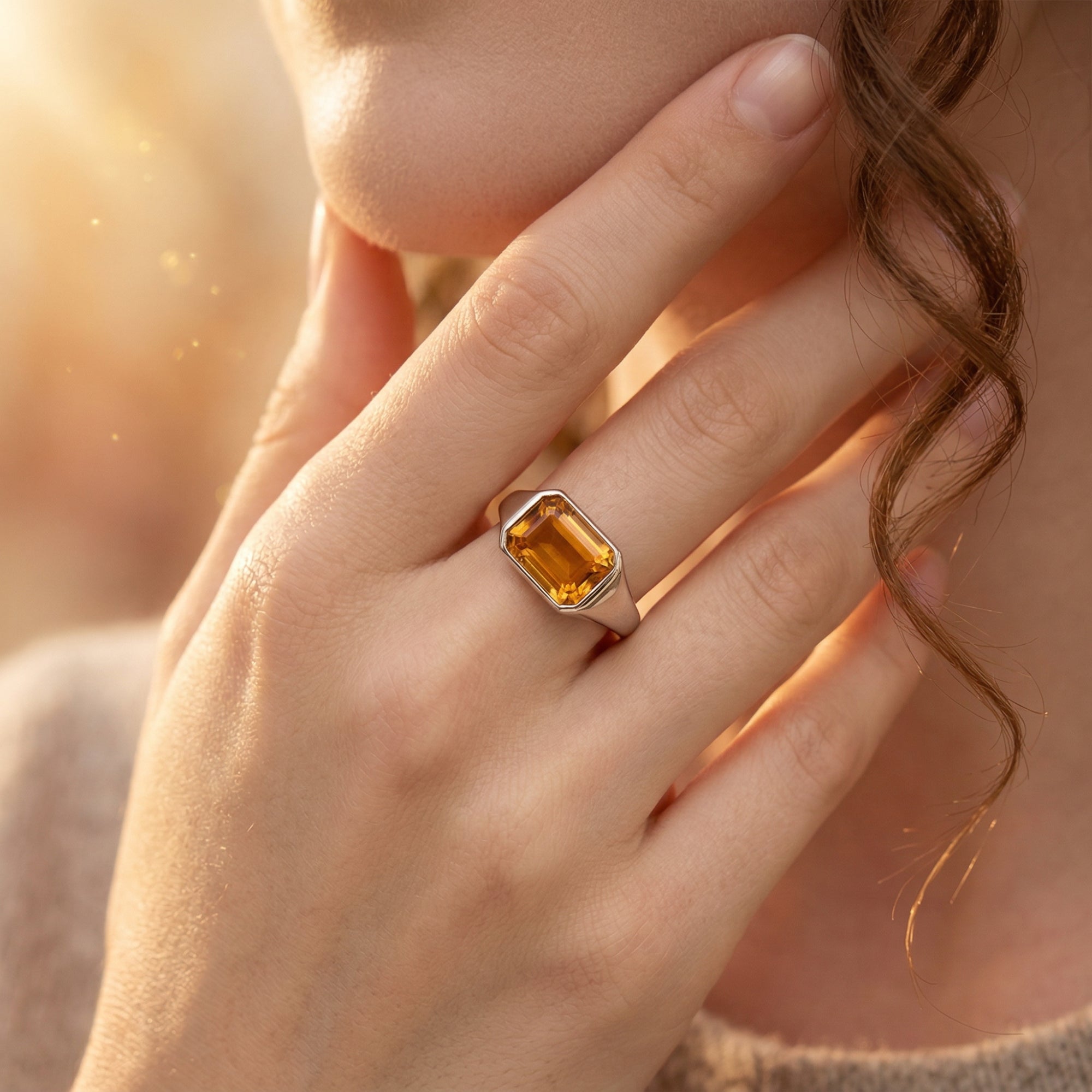 Emerald-cut natural citrine silver ring worn on a model's hand against a warm, sunlit background.