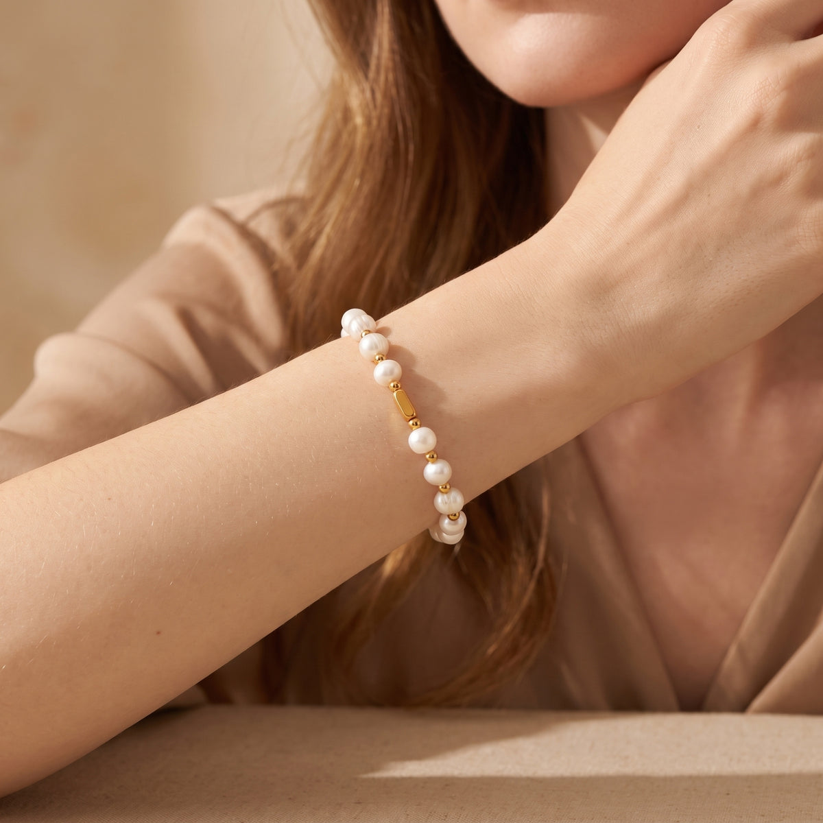 Model wearing the pearl station bracelet across her wrist with a warm neutral garment in the background.