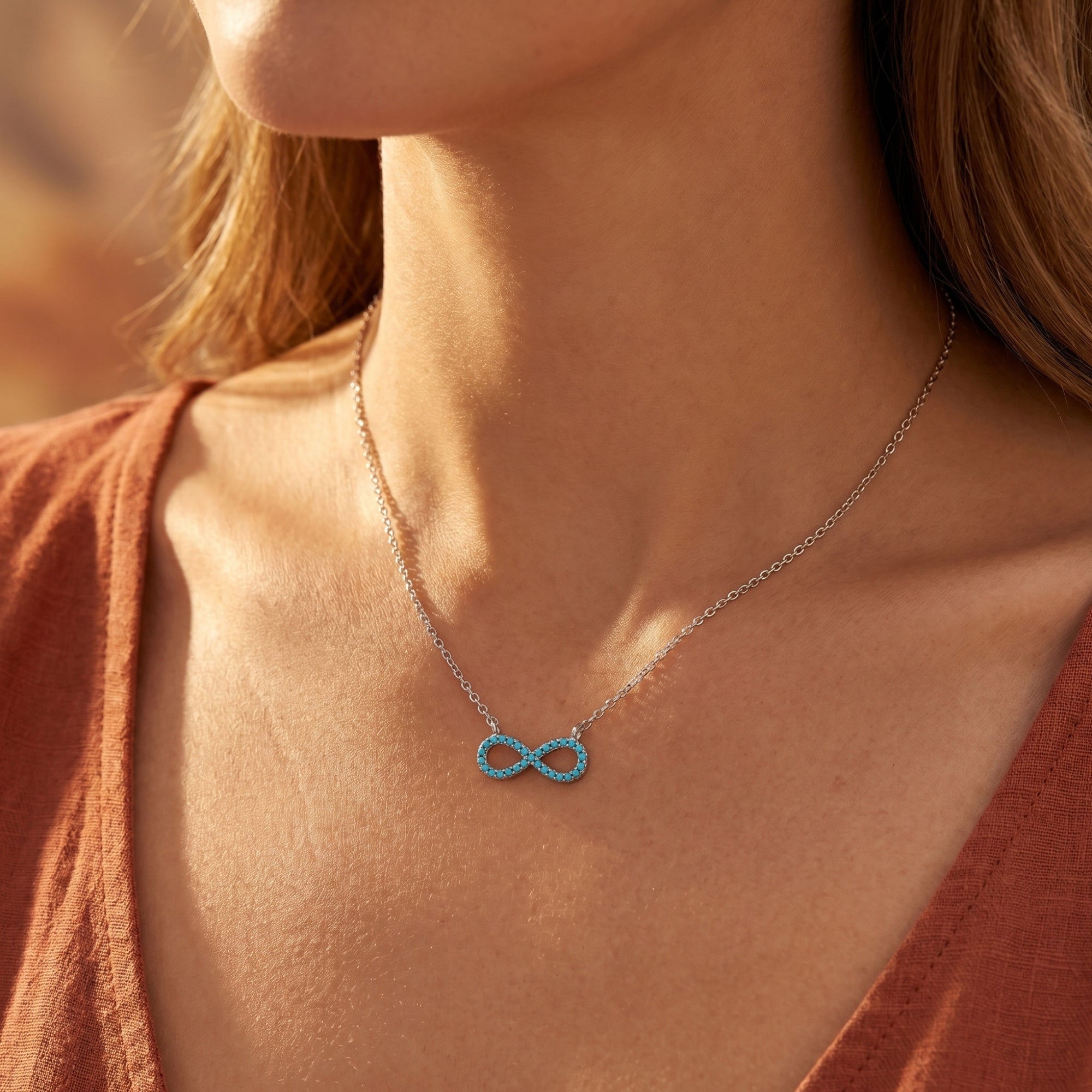 Silver infinity turquoise necklace worn by a model in a rust-colored top, showcasing the delicate chain and pendant.