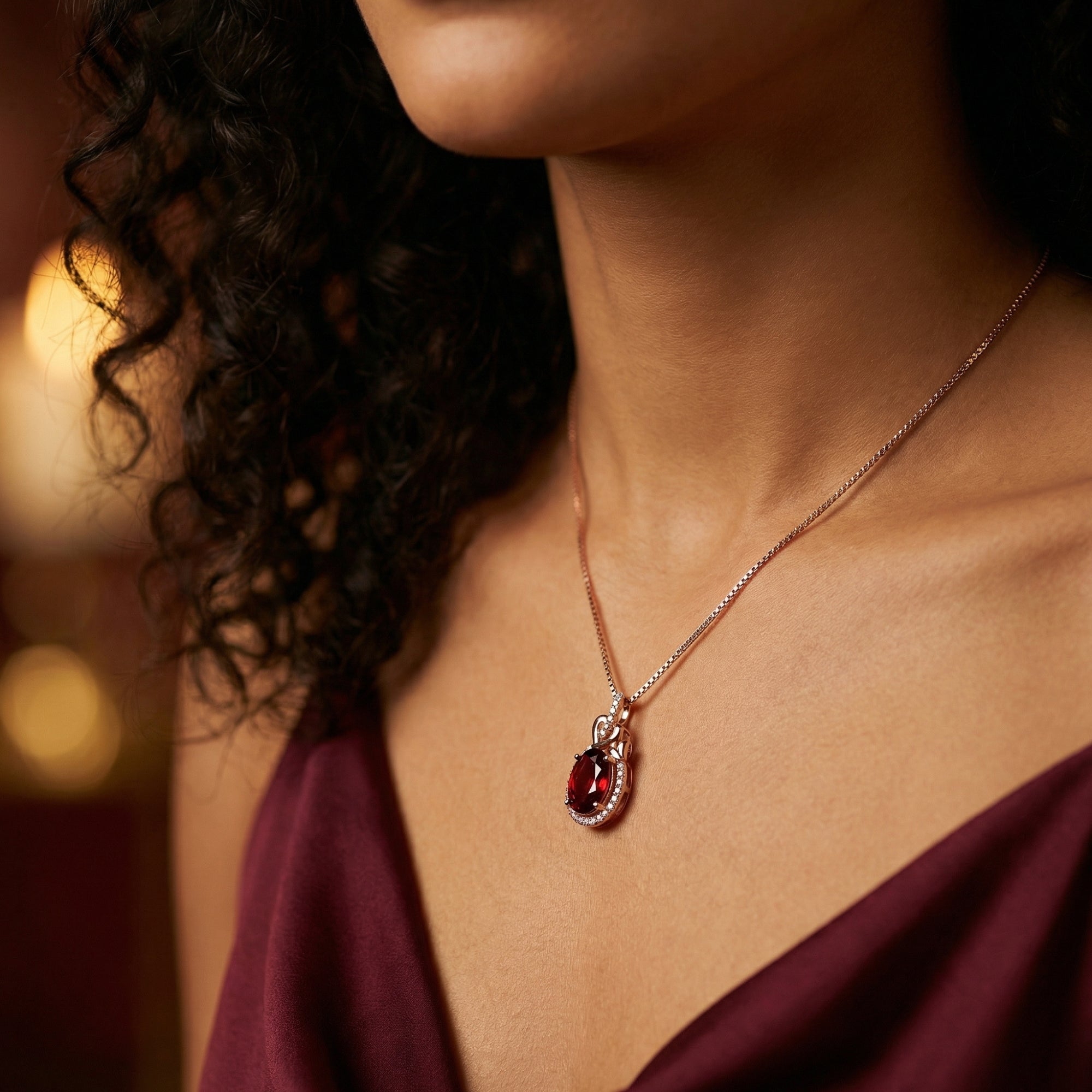 18K rose gold Cerys Halo Necklace with a natural oval garnet, worn by a model in a dark red dress.