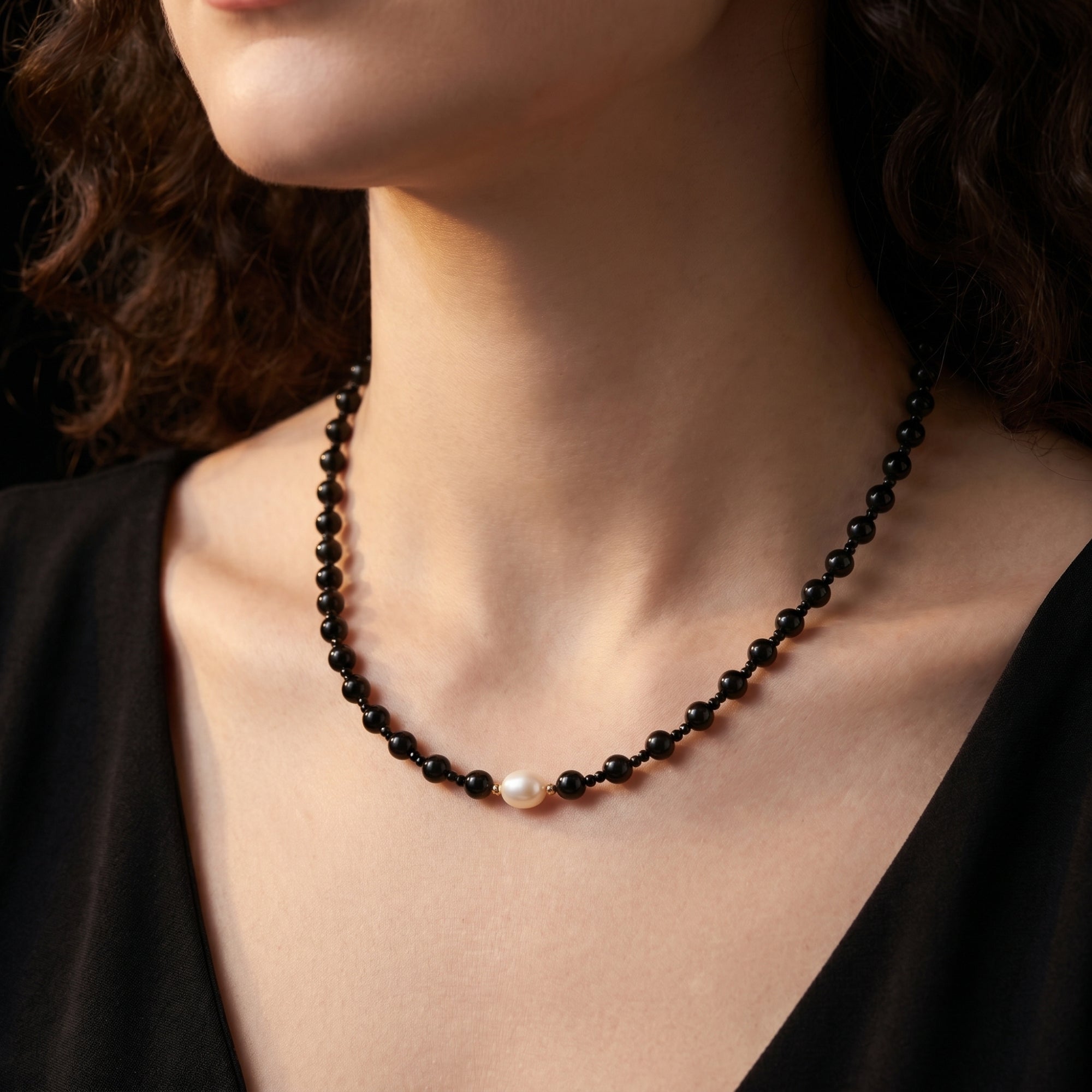 The Velvet Onyx and Pearl Necklace in 18K gold plating worn by a woman in a black dress.