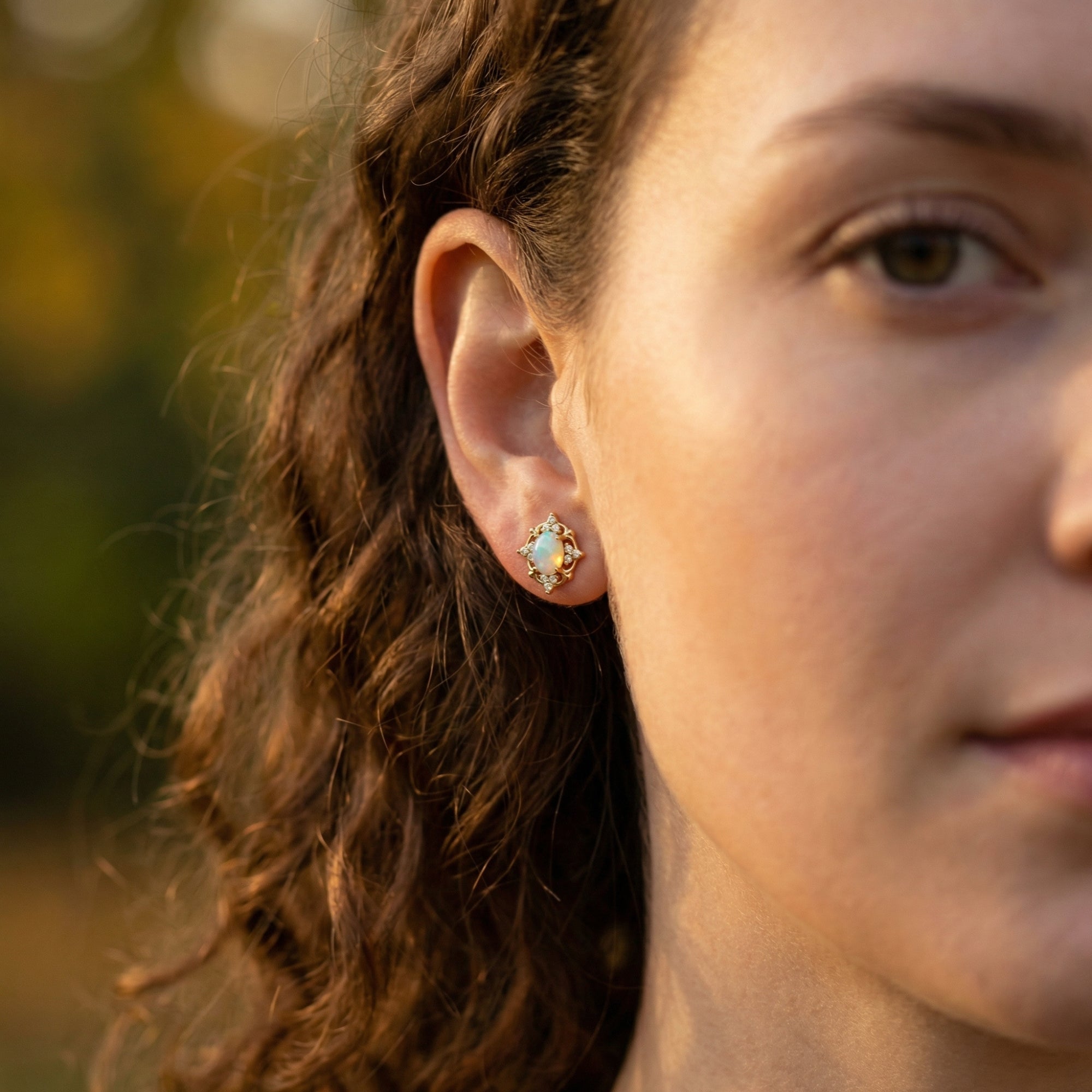Side view of a woman wearing a gold-tone white opal filigree earring in a natural outdoor setting.