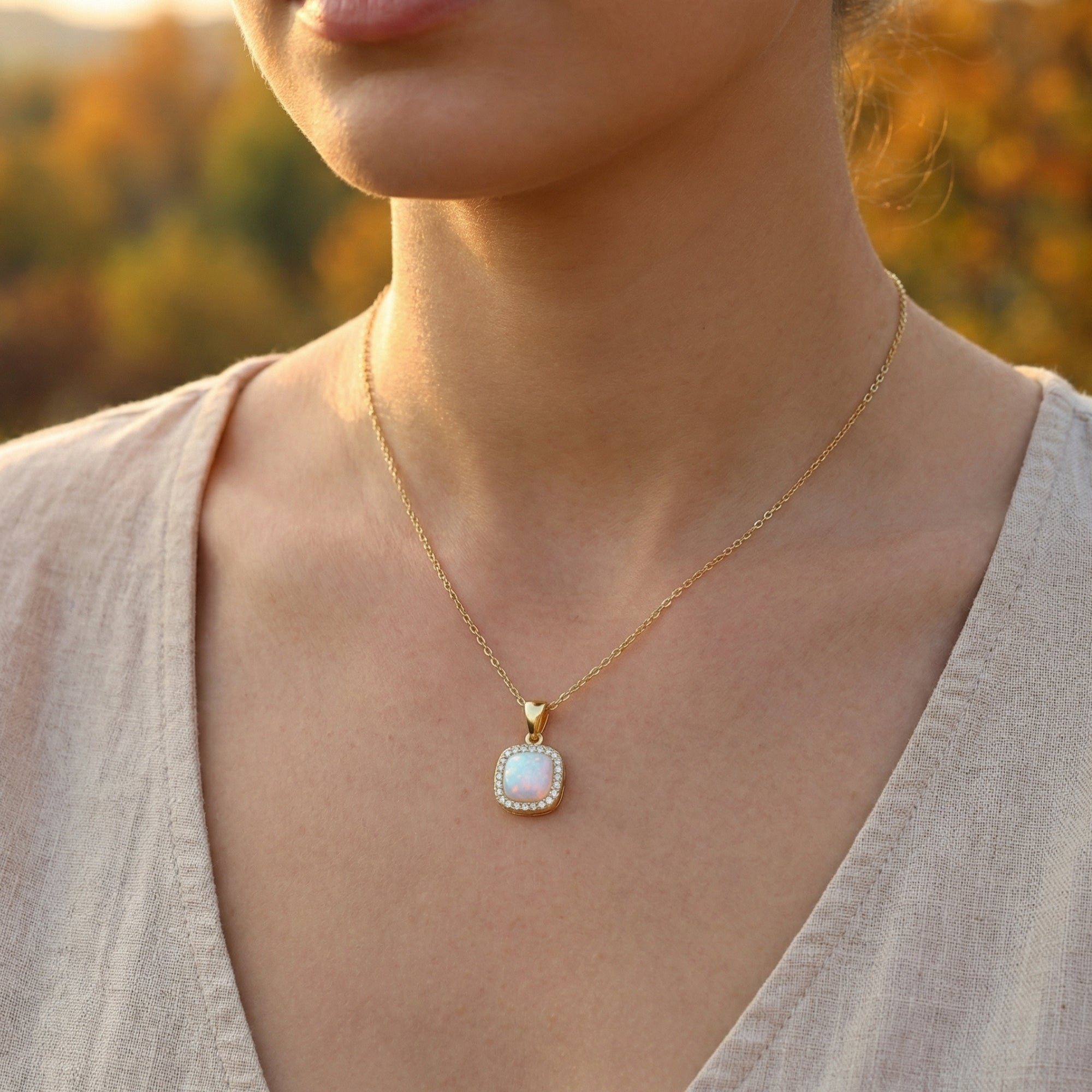 Close-up of a woman wearing the gold cushion cut white opal halo pendant necklace in natural light.