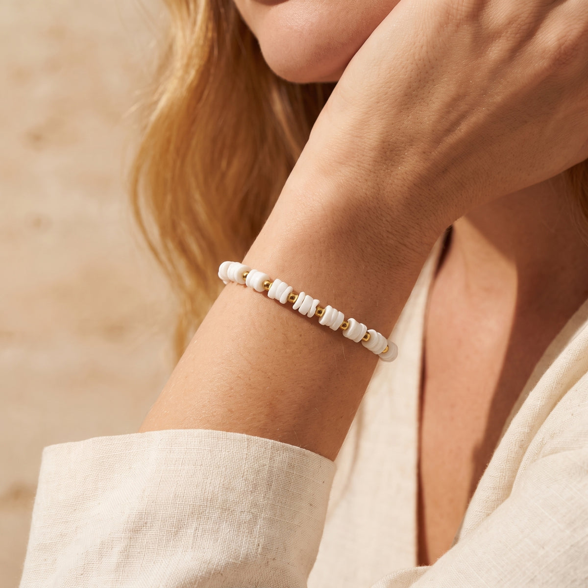 Side view of the white disc-bead bracelet with gold-tone spacers worn on a wrist beside a cream sleeve.