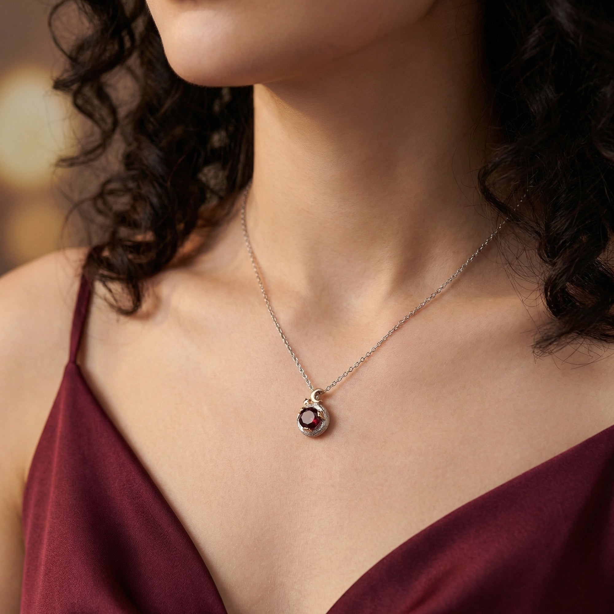 A woman wearing the Ember round garnet pendant necklace in silver, showing the chain and celestial pendant design.