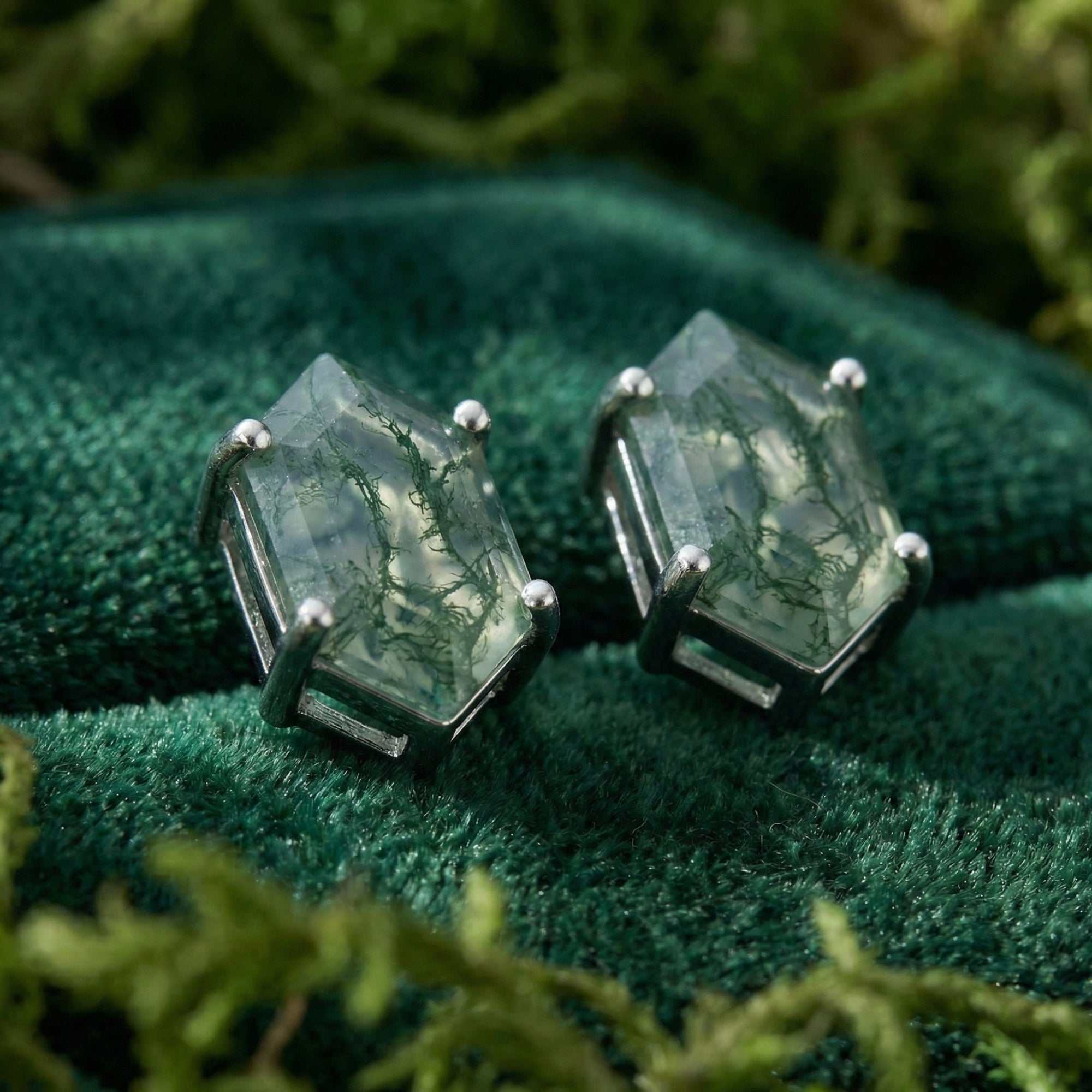 Macro view of sterling silver prongs holding hexagon-cut moss agate stones on a green velvet background.