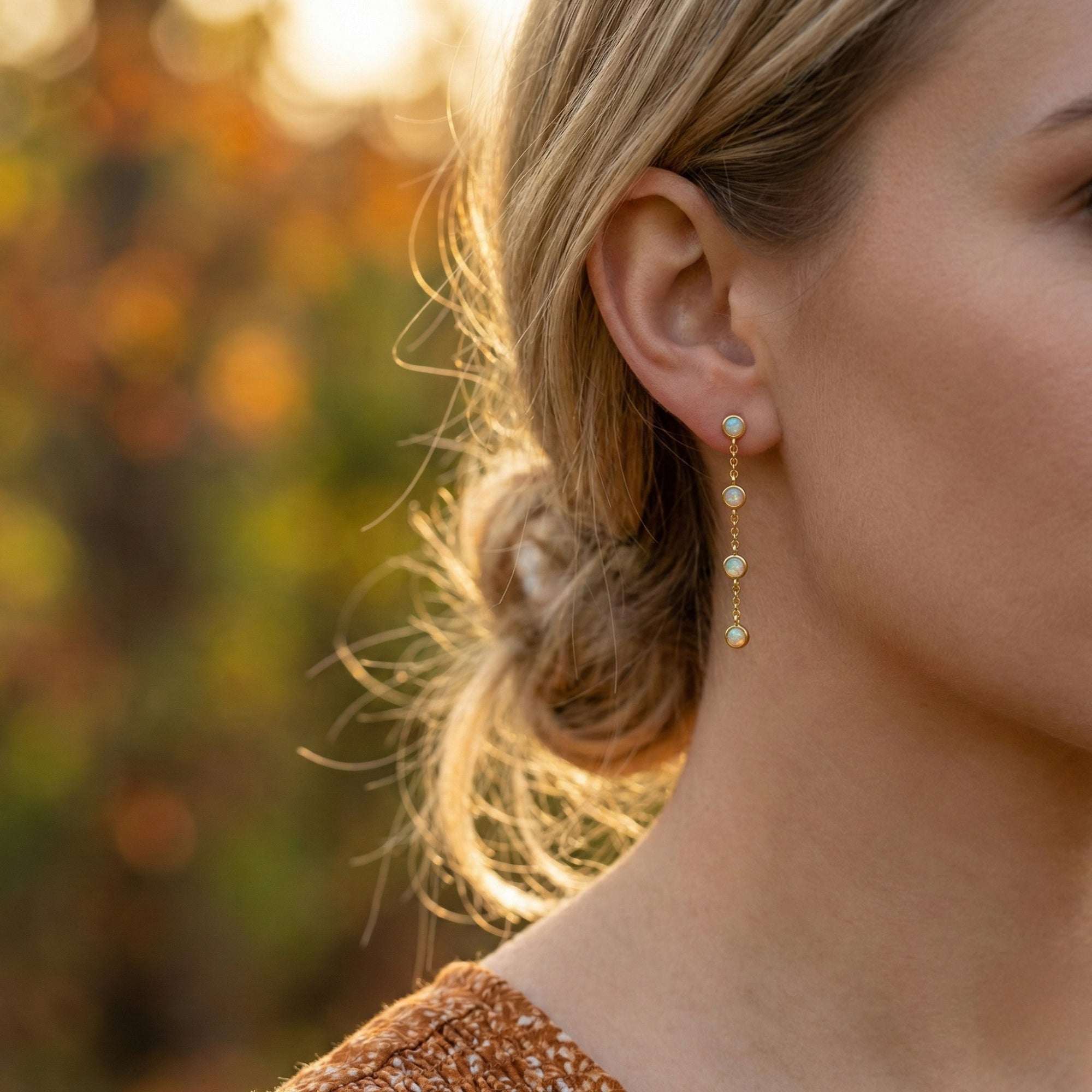 Side profile of a woman wearing the Arianell gold drop earrings with four white opals in a linear cascade.
