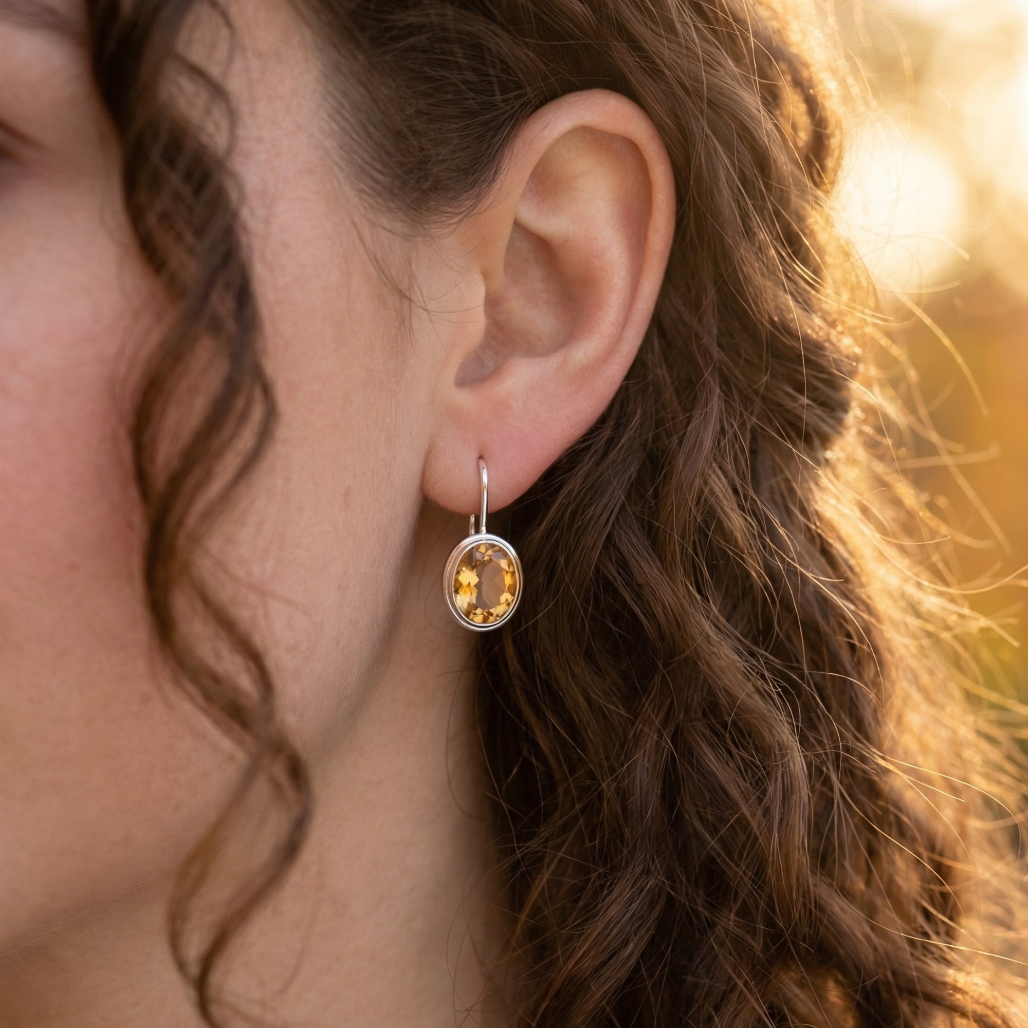 Close-up view of a sterling silver oval natural citrine drop earring worn on a model's ear.