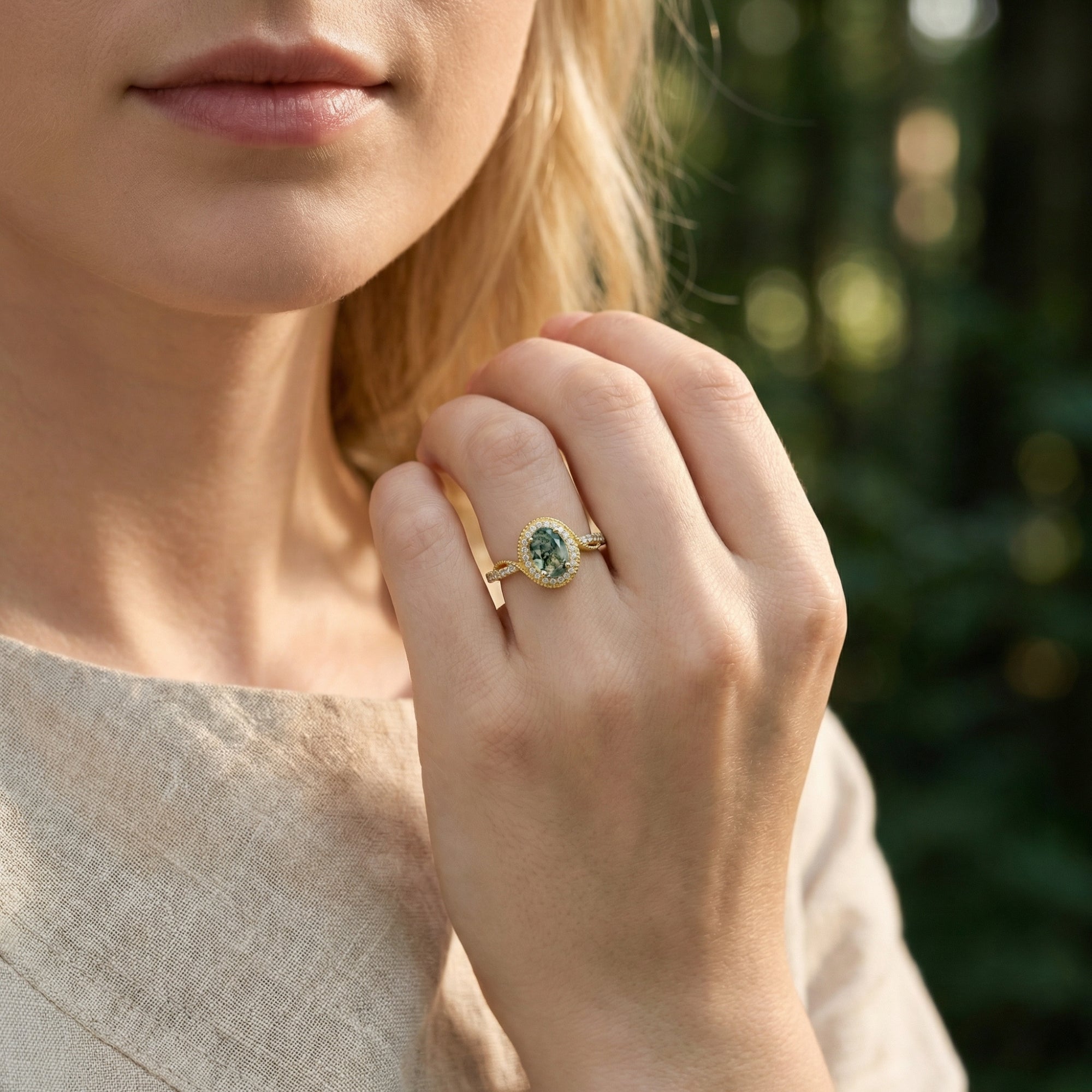 Close-up of a gold halo moss agate ring on a model's hand, highlighting the oval cut stone and pavé band.