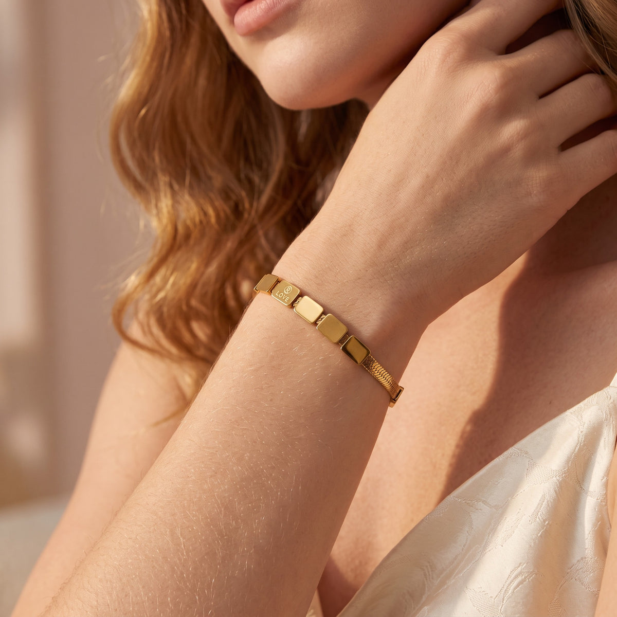 Close-up of a gold-tone tile bracelet worn on a wrist, with one visible tile engraved “LOVE.”