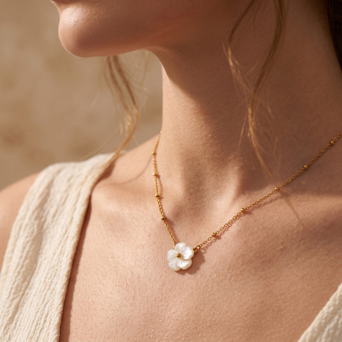 Side-angle view of a gold-tone bead-station necklace with a carved white flower pendant worn on a model.