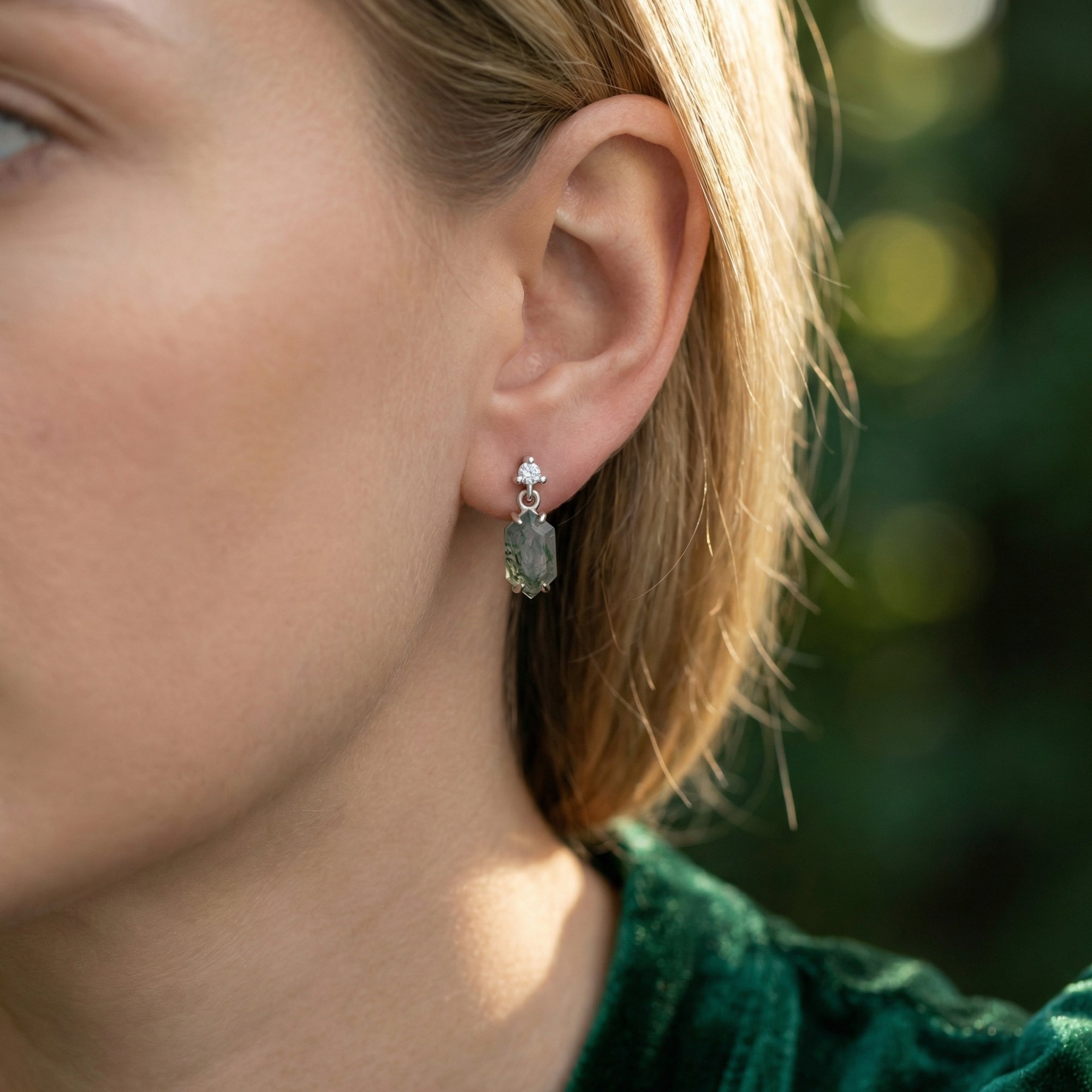 Model wearing a barrel cut natural moss agate dangle earring in sterling silver, showing scale and fit.
