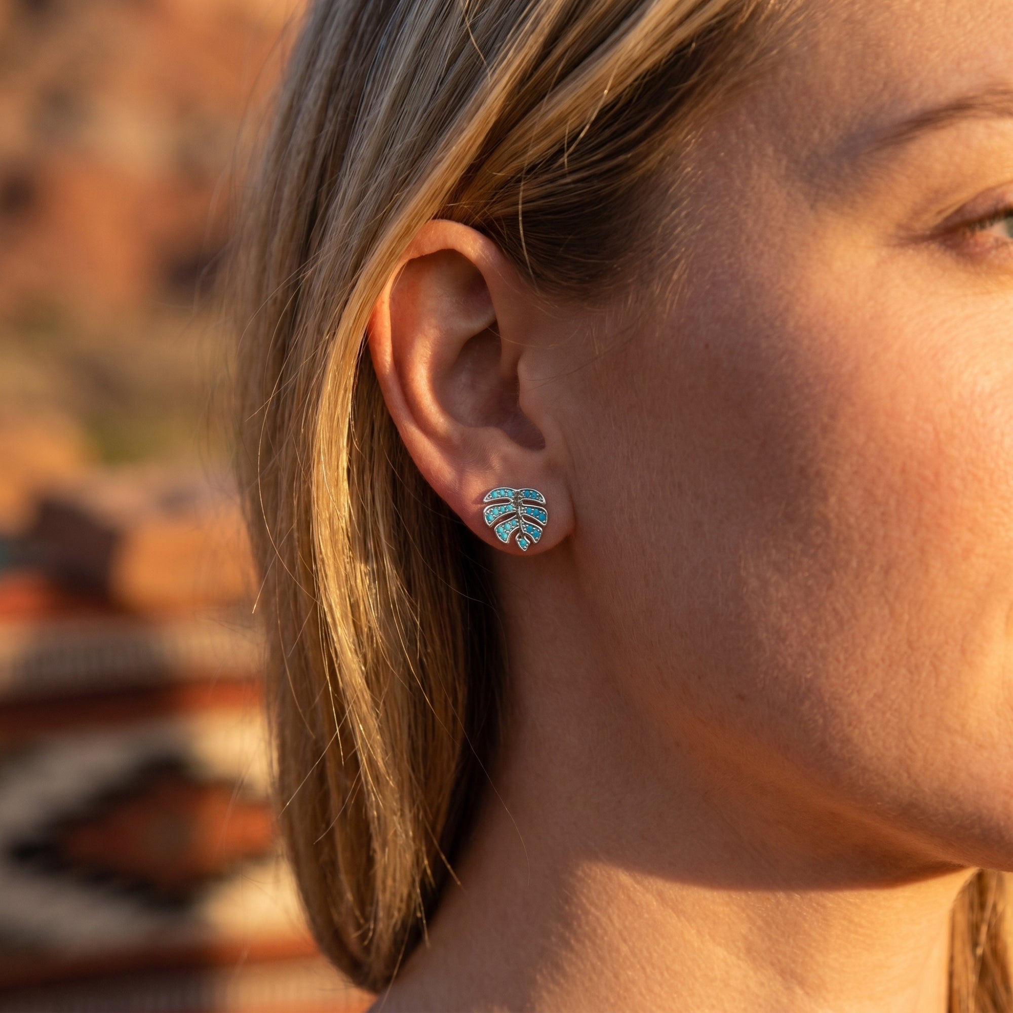 Profile view of a woman wearing a silver monstera leaf turquoise earring in a desert setting.