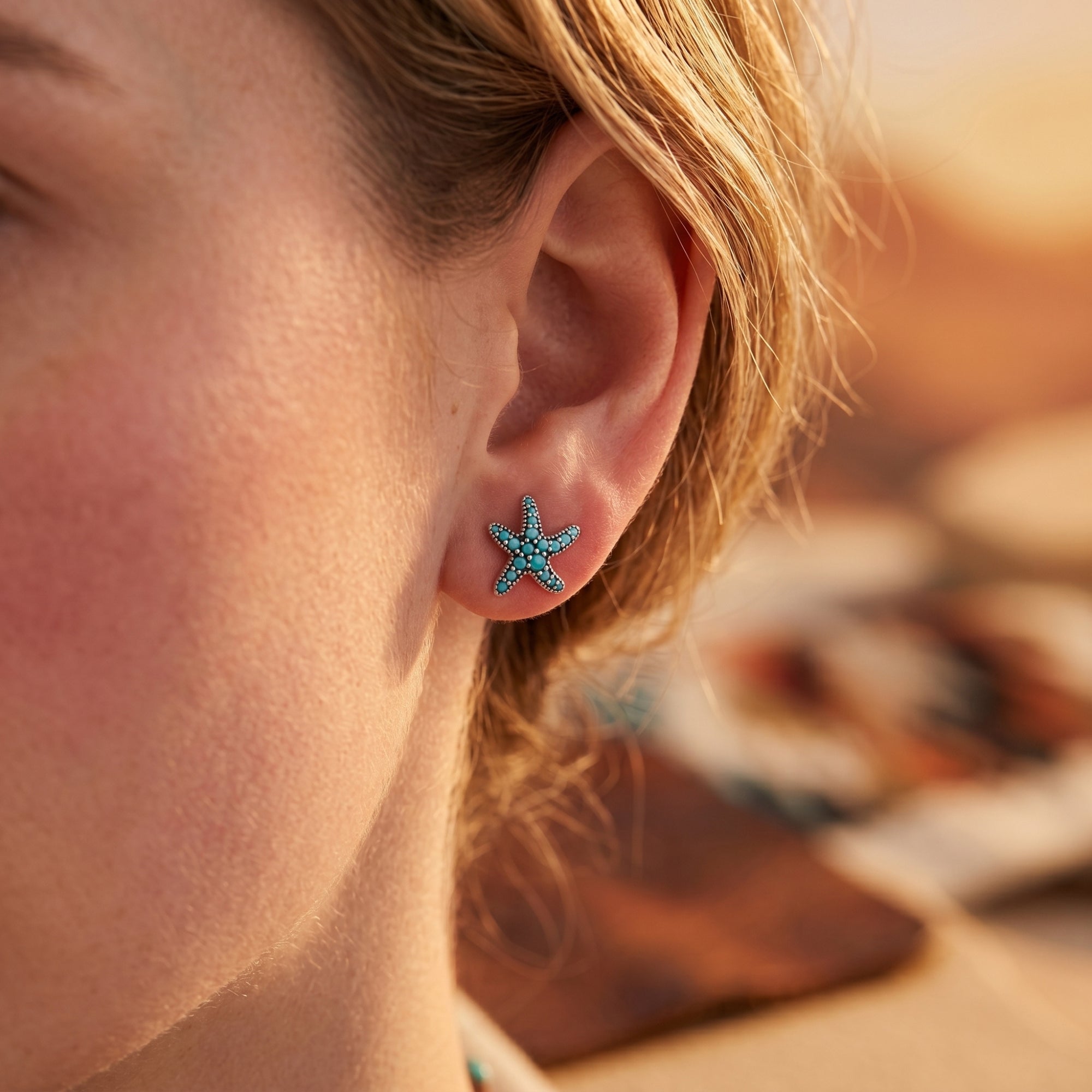 Close-up of a turquoise and sterling silver starfish stud earring worn on a woman's ear.