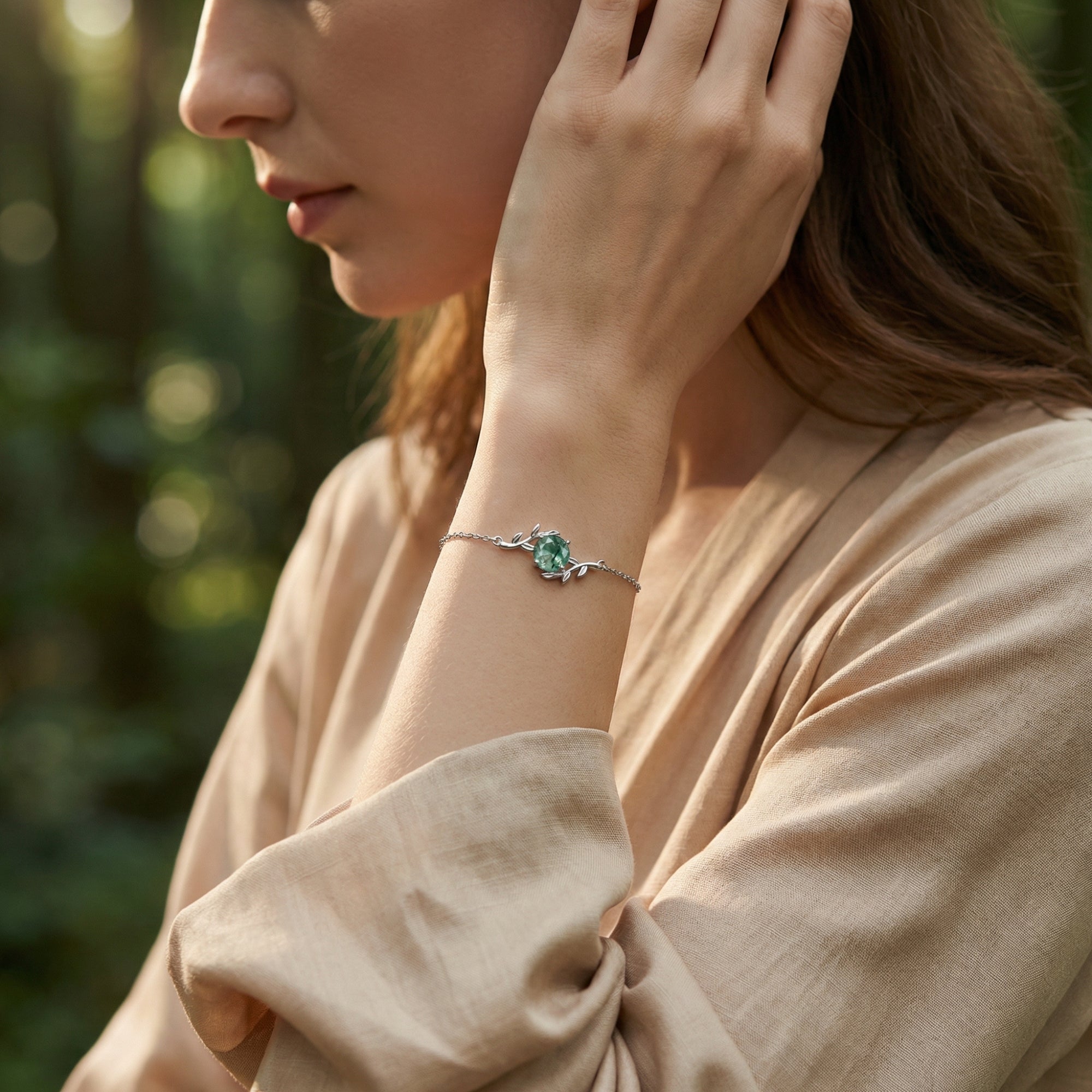 Sterling silver vine wrap bracelet with a green moss agate stone worn on a model's wrist in soft outdoor light.