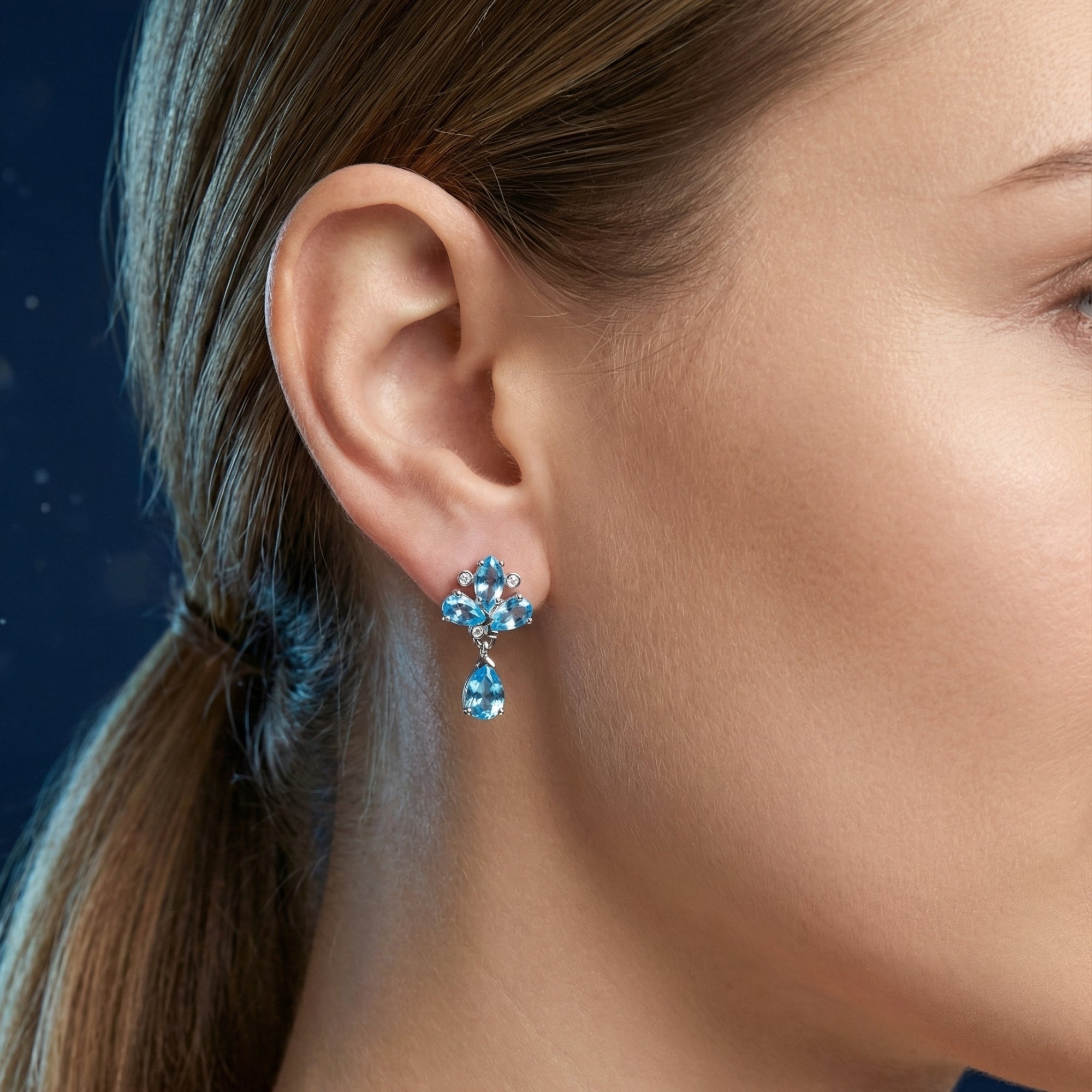 Profile view of a woman wearing silver drop earrings with pear cut Swiss blue topaz.