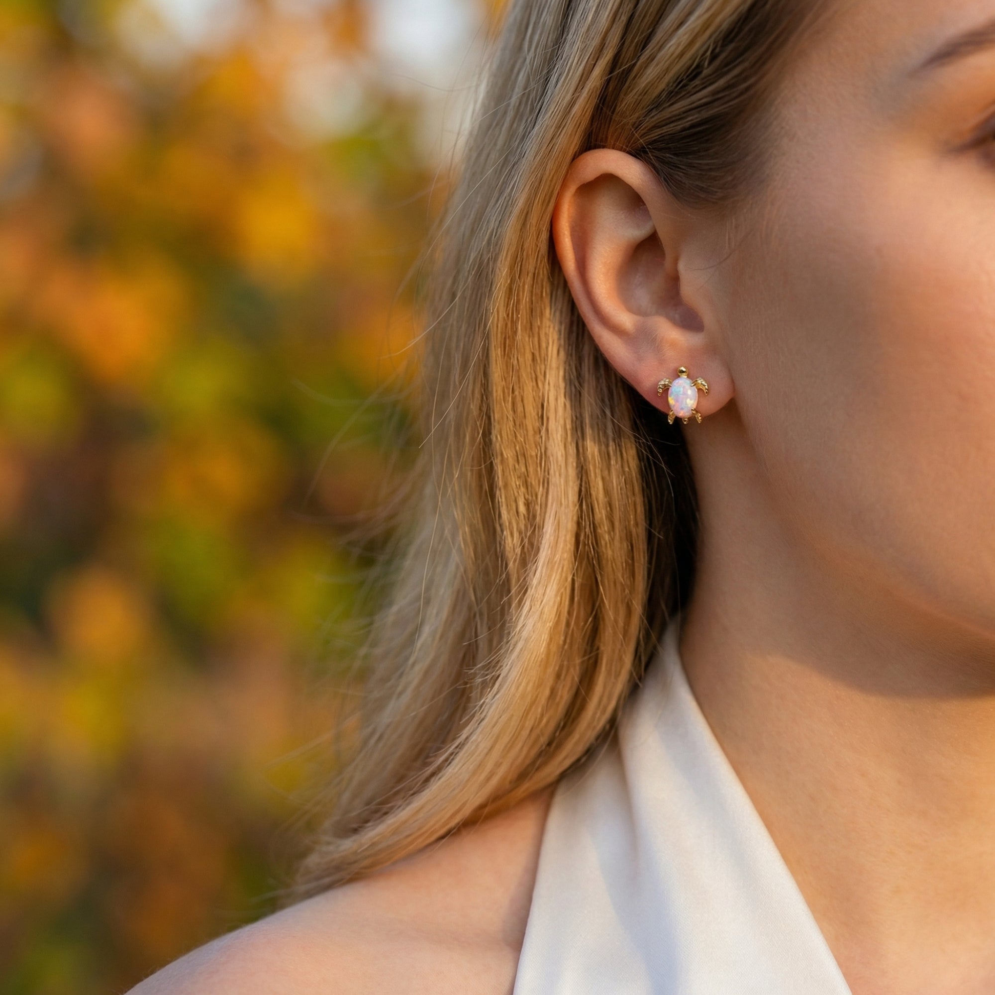 Side view of a woman wearing a gold-tone turtle stud earring with a white opal gemstone.