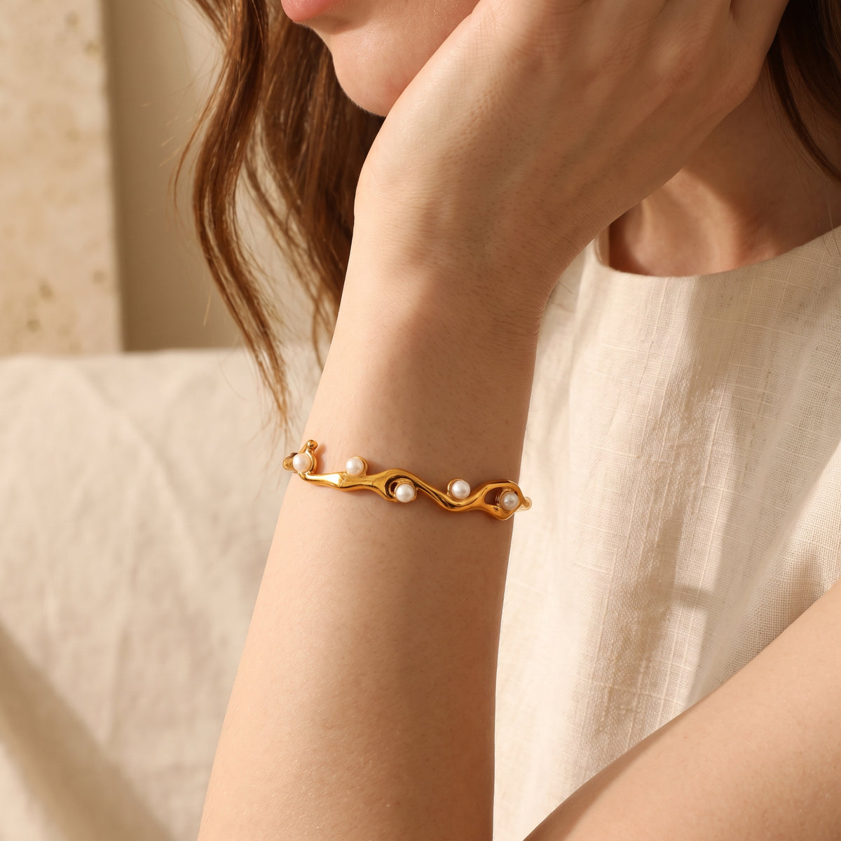 Model wearing a gold-tone wave pearl cuff bracelet on her wrist with her hand near her chin.